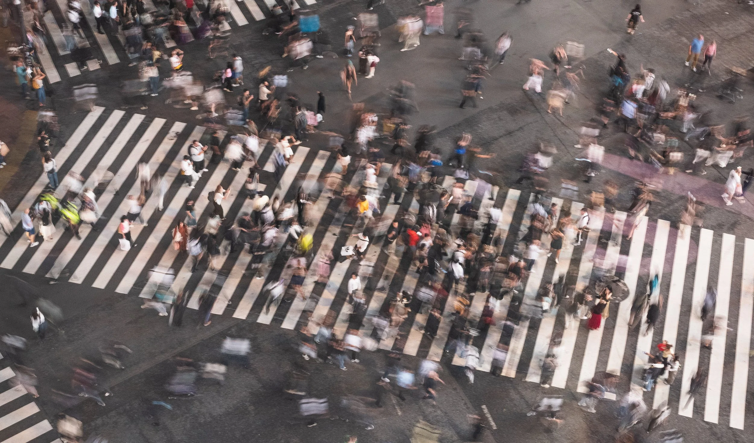 Crowded crosswalk at night with blurred pedestrians walking across the street.