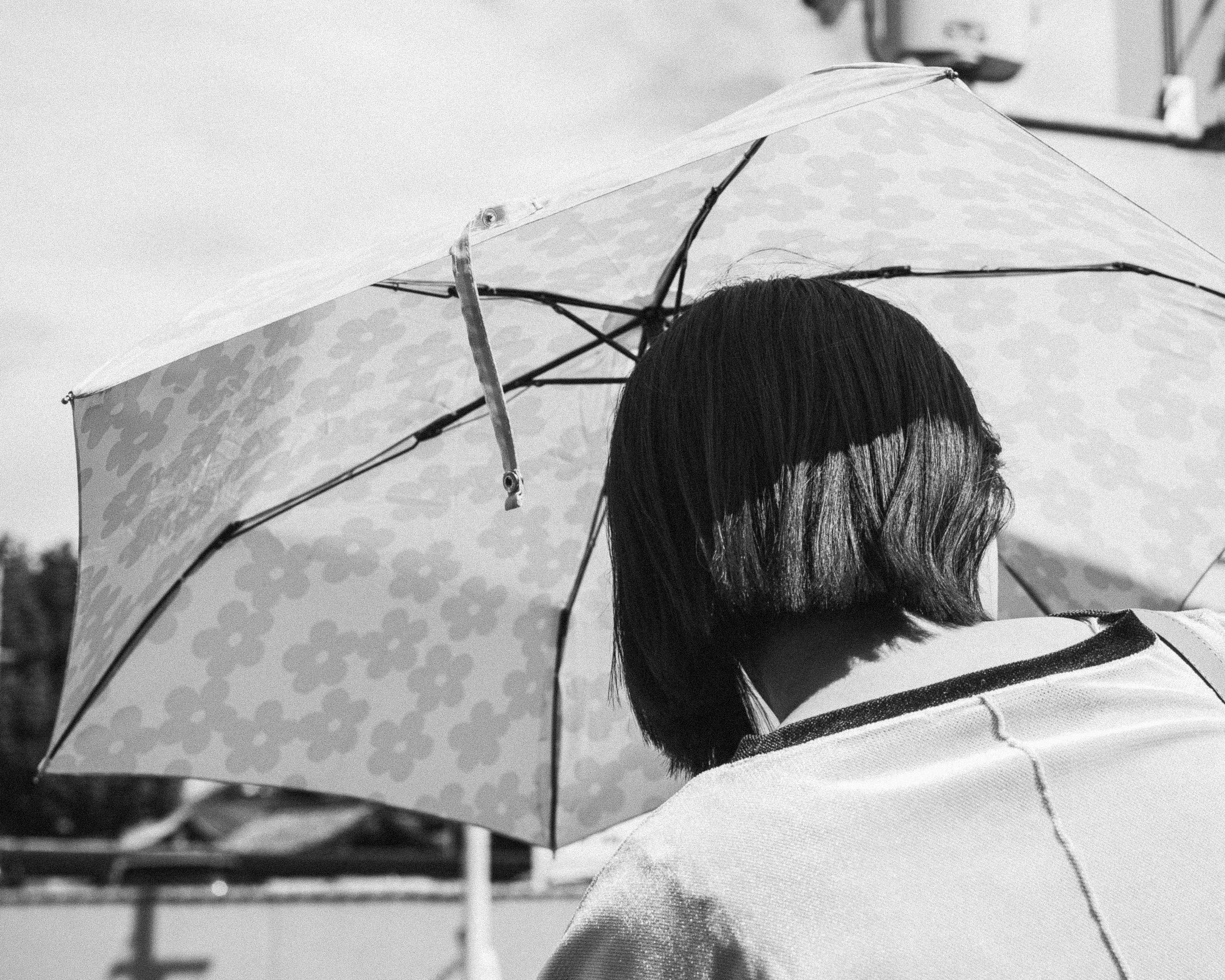 A person with shoulder-length dark hair holding an umbrella with a floral pattern, viewed from behind.