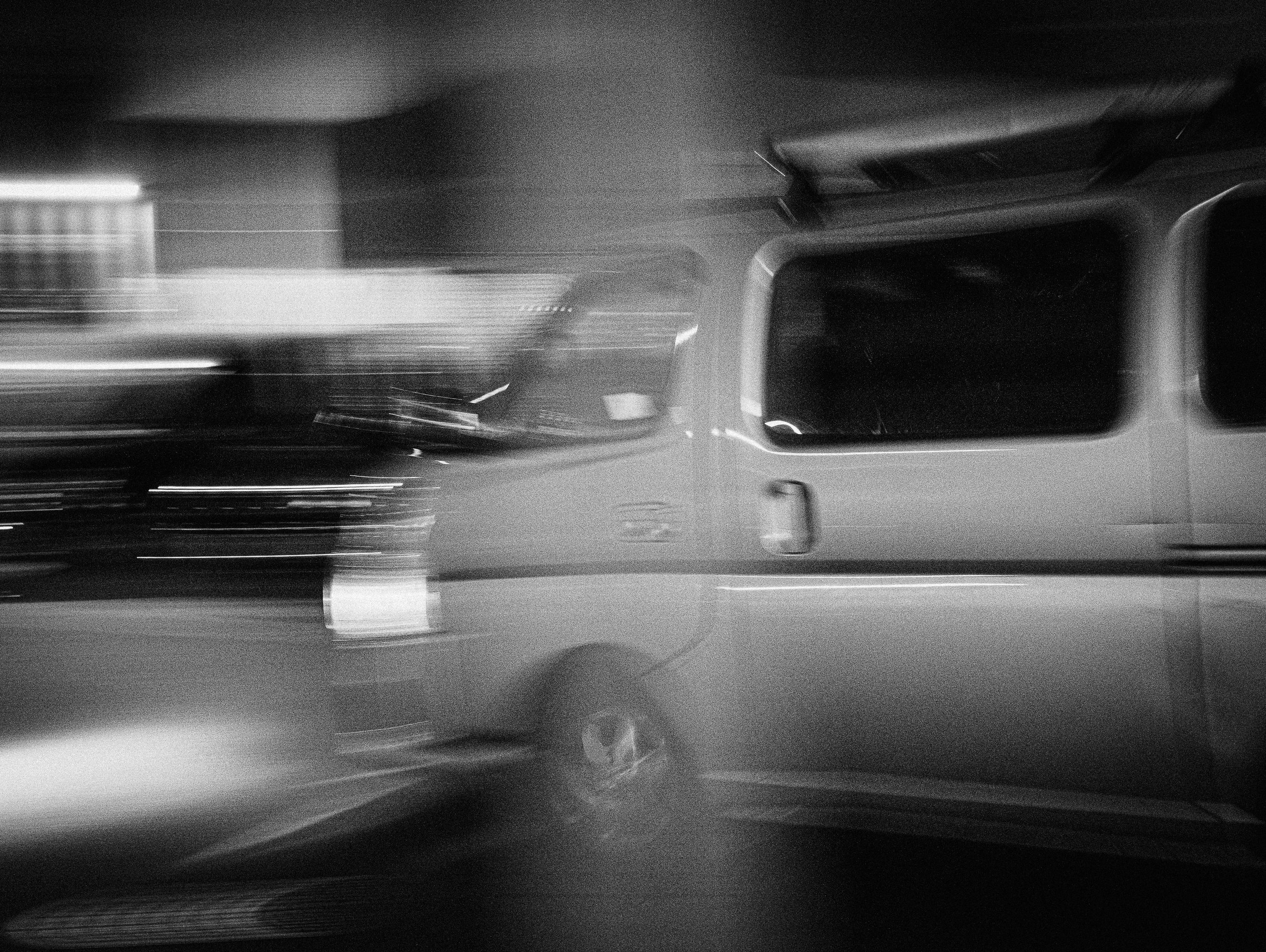 Black and white photo of a blurred van in motion at night.