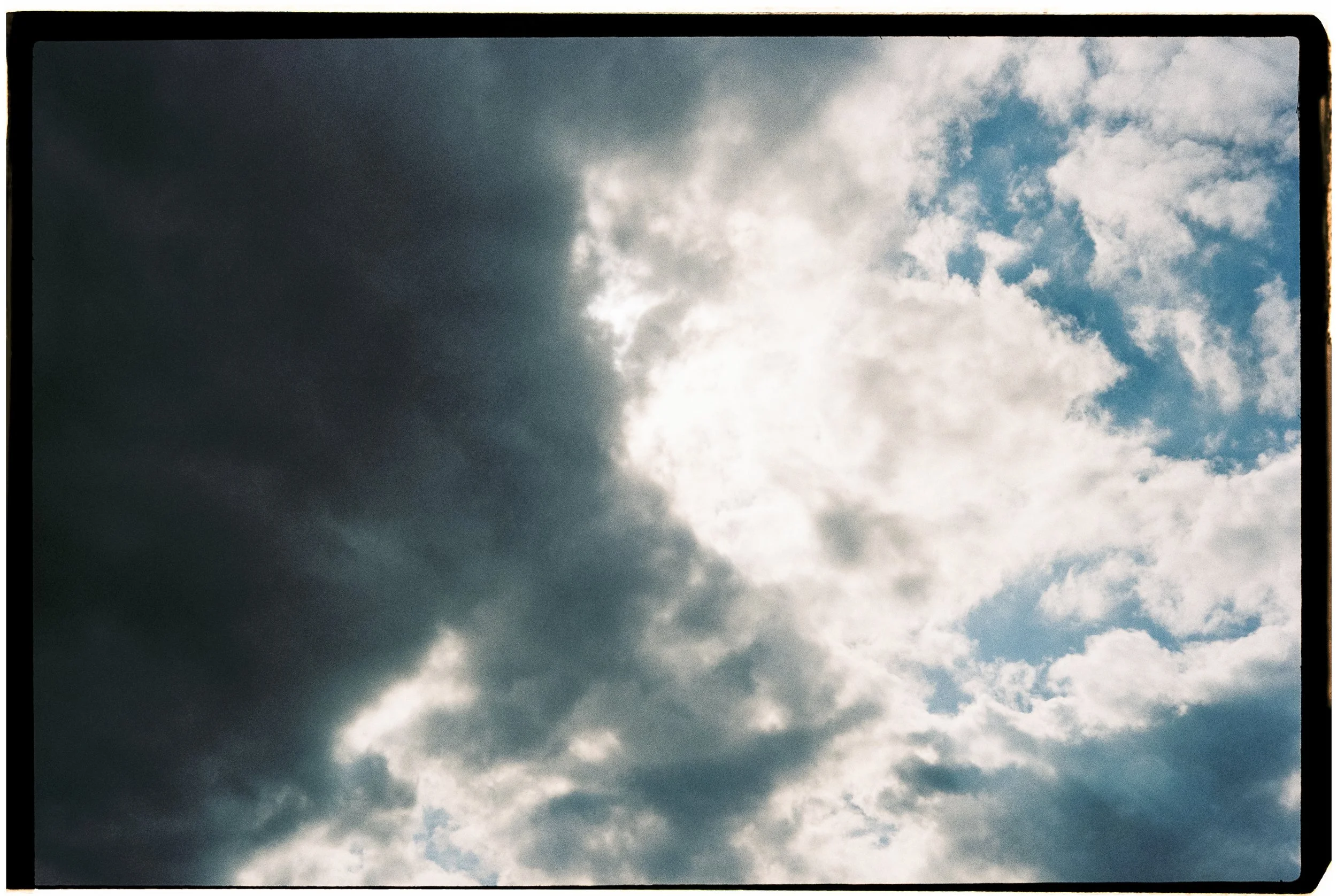 Partially cloudy sky with the sun behind dark and light clouds.