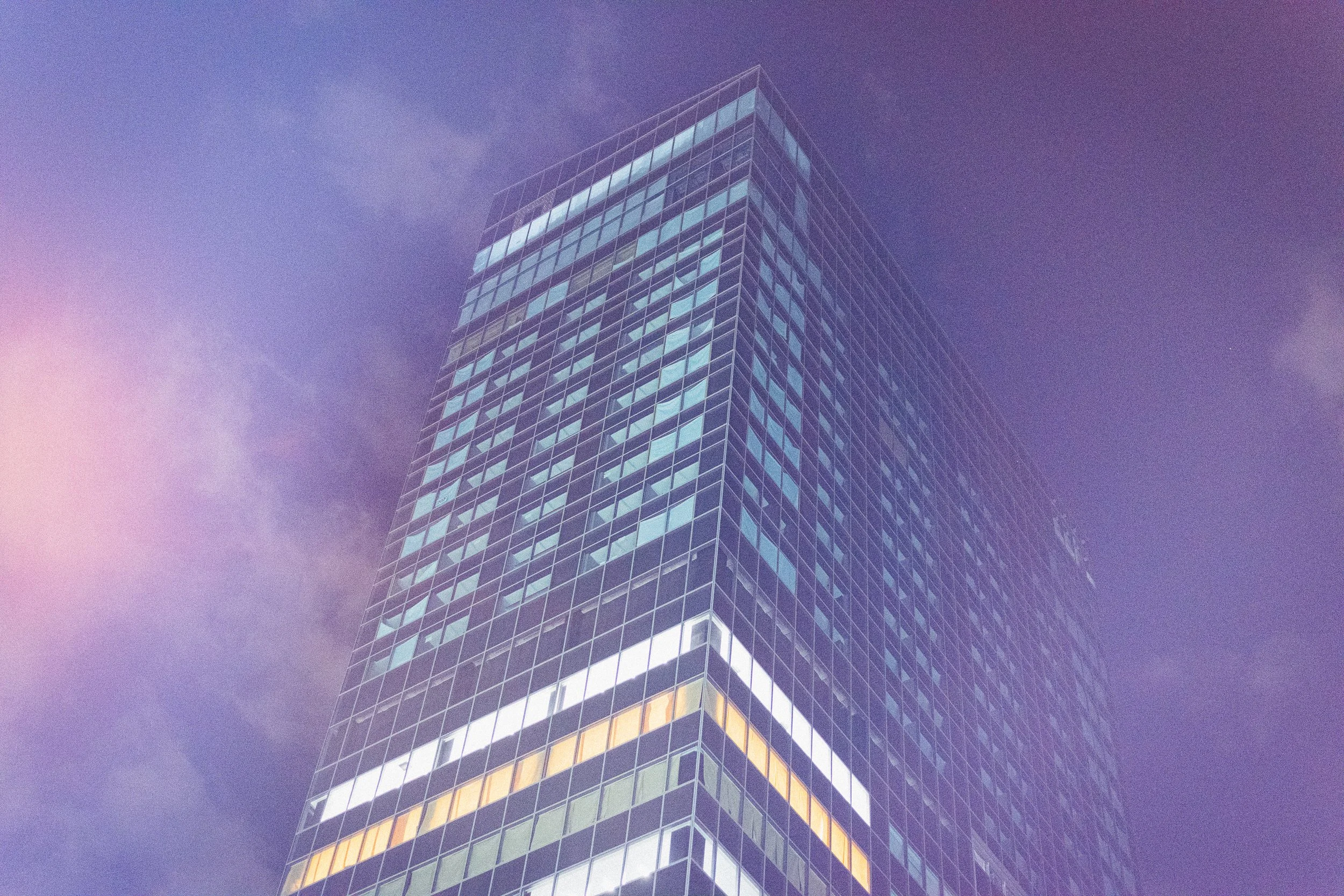 A tall modern glass skyscraper with reflective windows, against a purple-tinged sky.