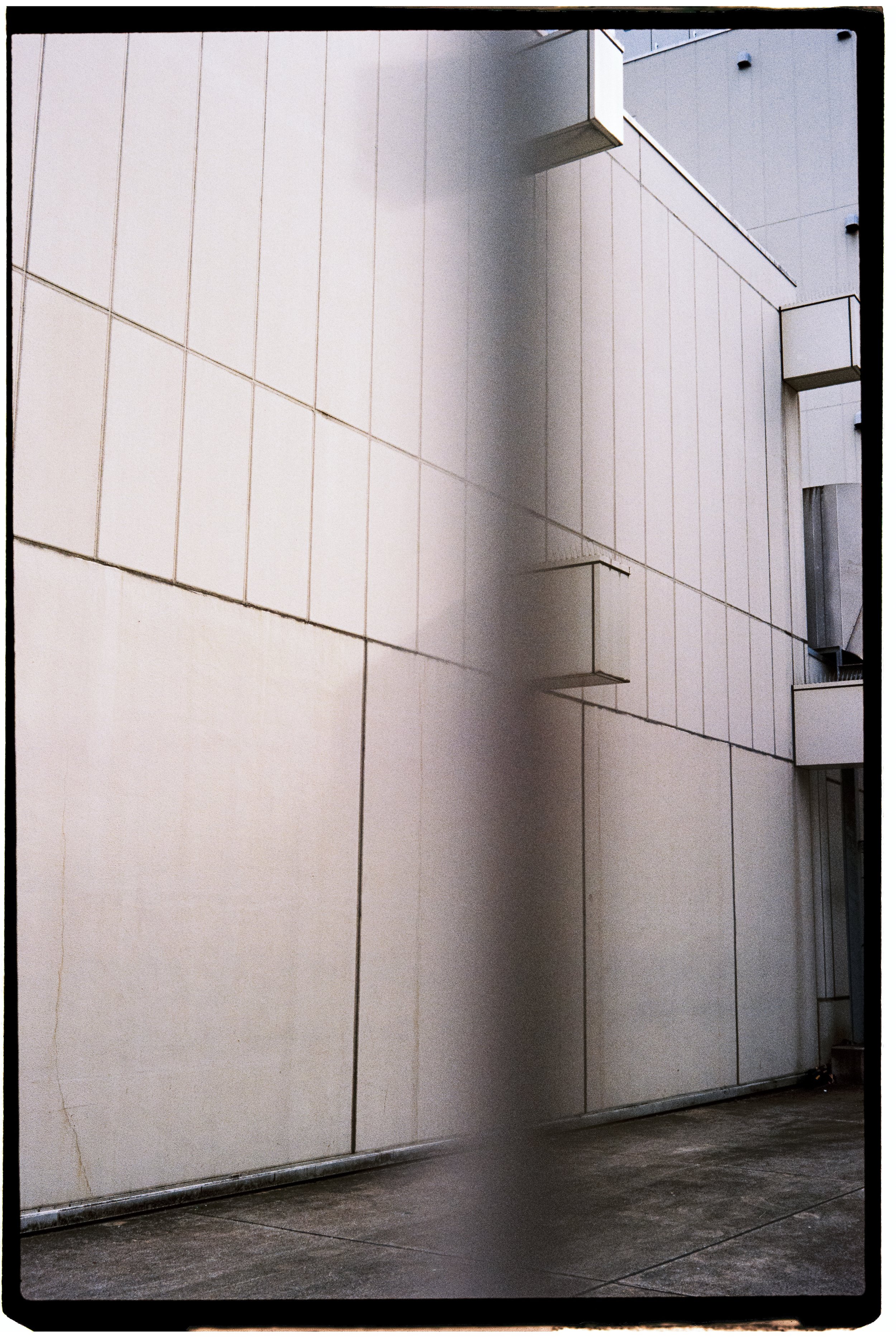 Exterior view of a modern building with beige tiled walls, a narrow vertical shadow, and small rectangular balconies.