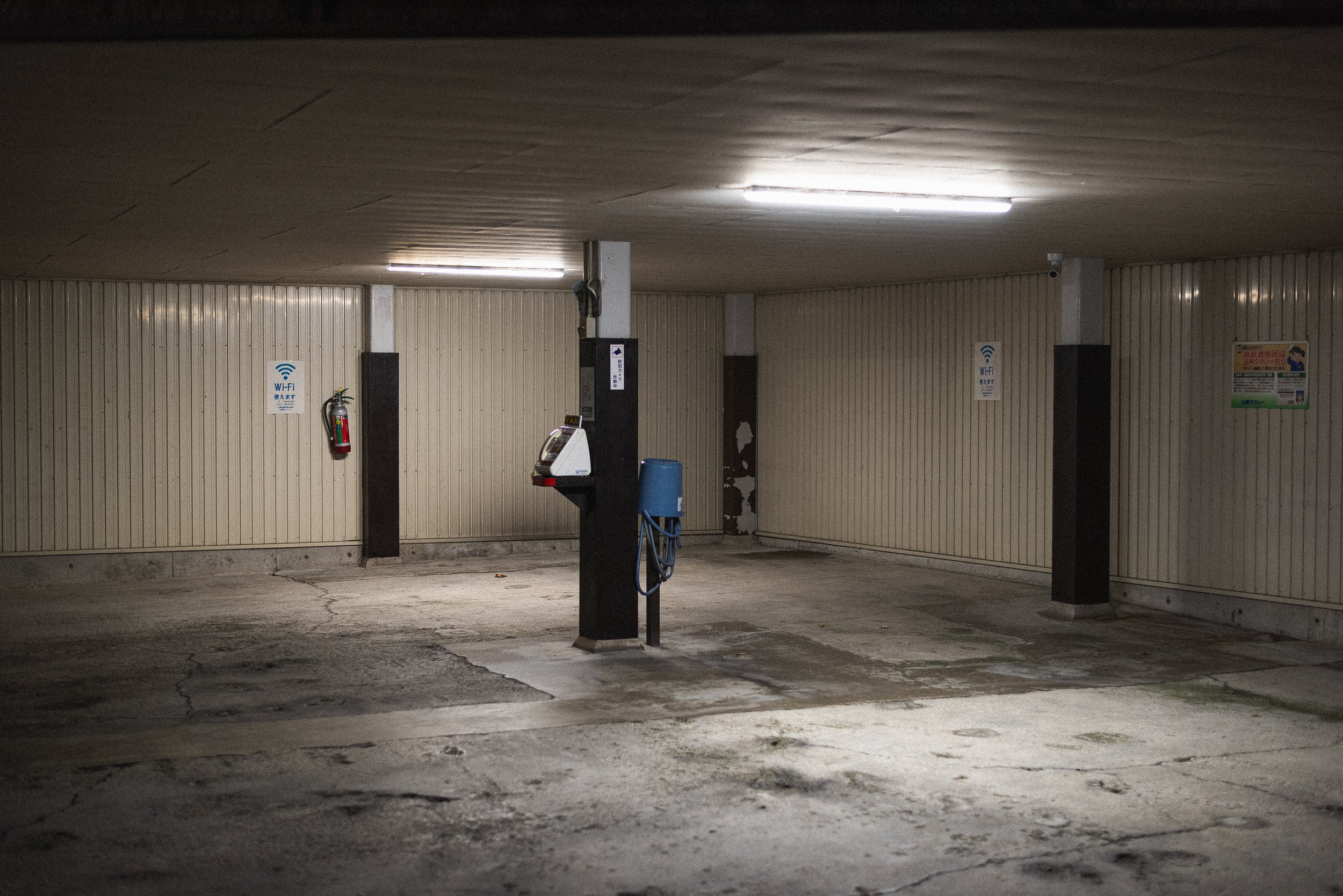 Empty indoor parking garage with concrete floor and beige paneled walls, featuring a payphone and a fire extinguisher.