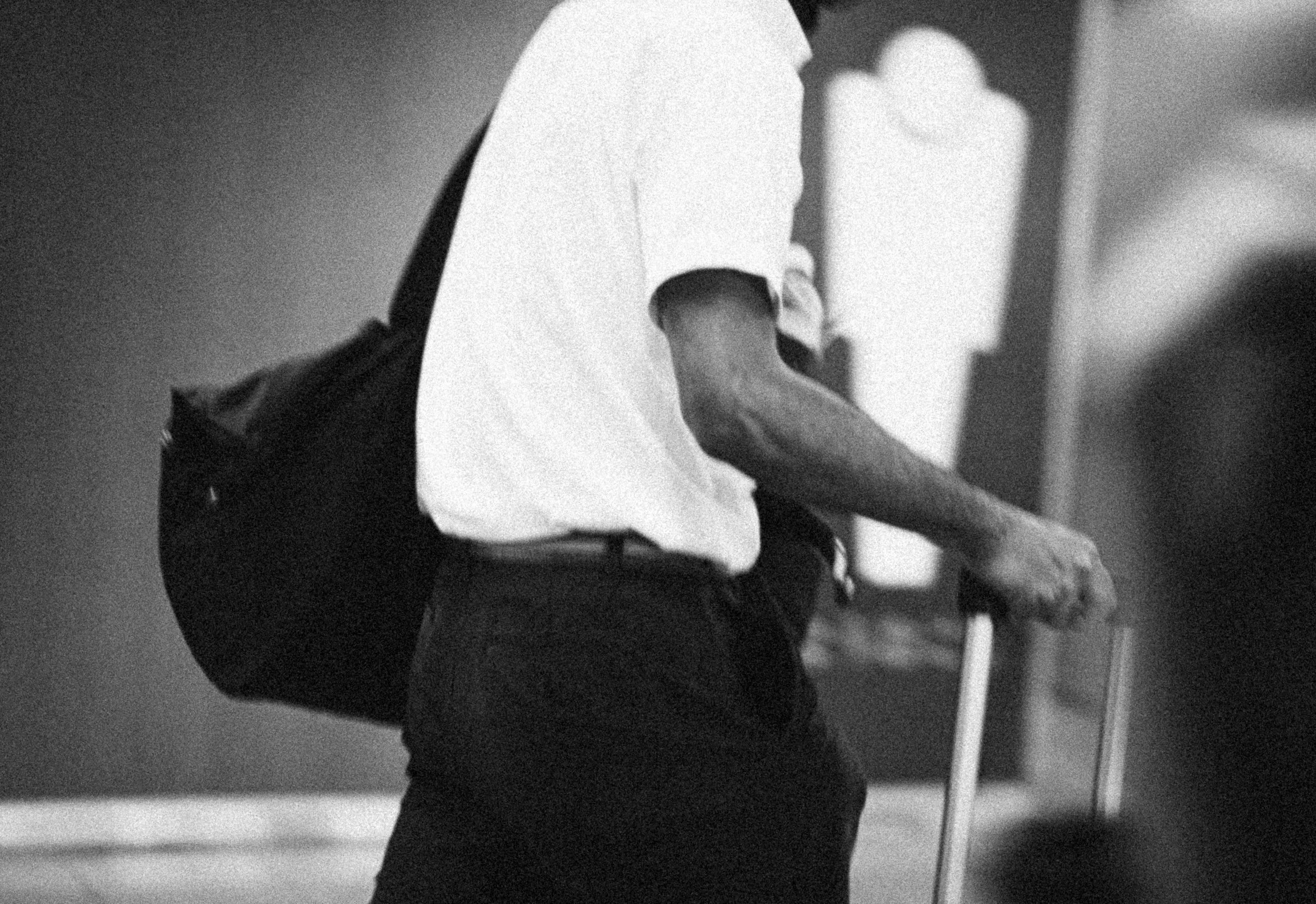 Person with a backpack, wearing a white shirt, using a cane.