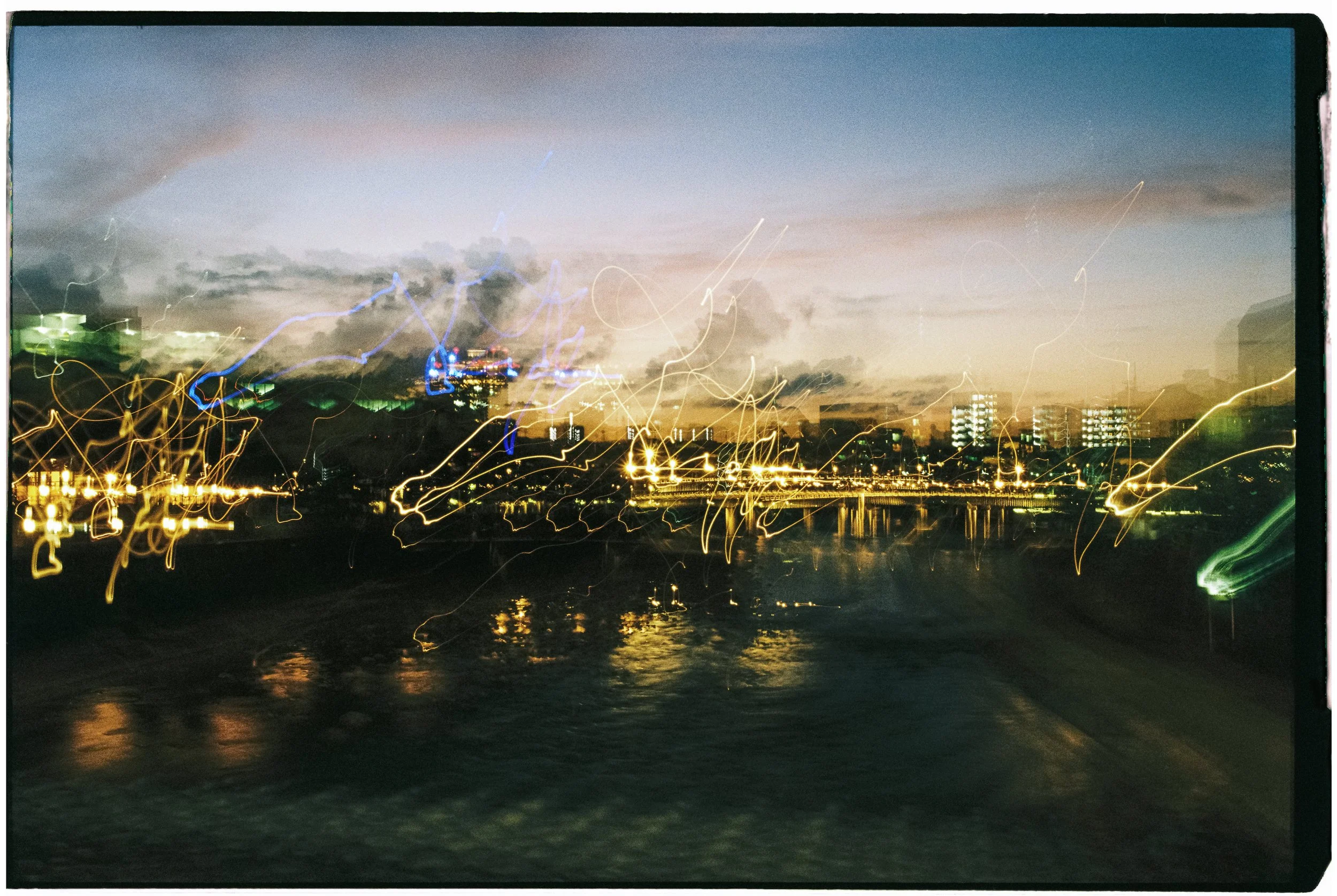 City skyline at dusk with streaks of light from moving vehicles and decorative city lights in the foreground.