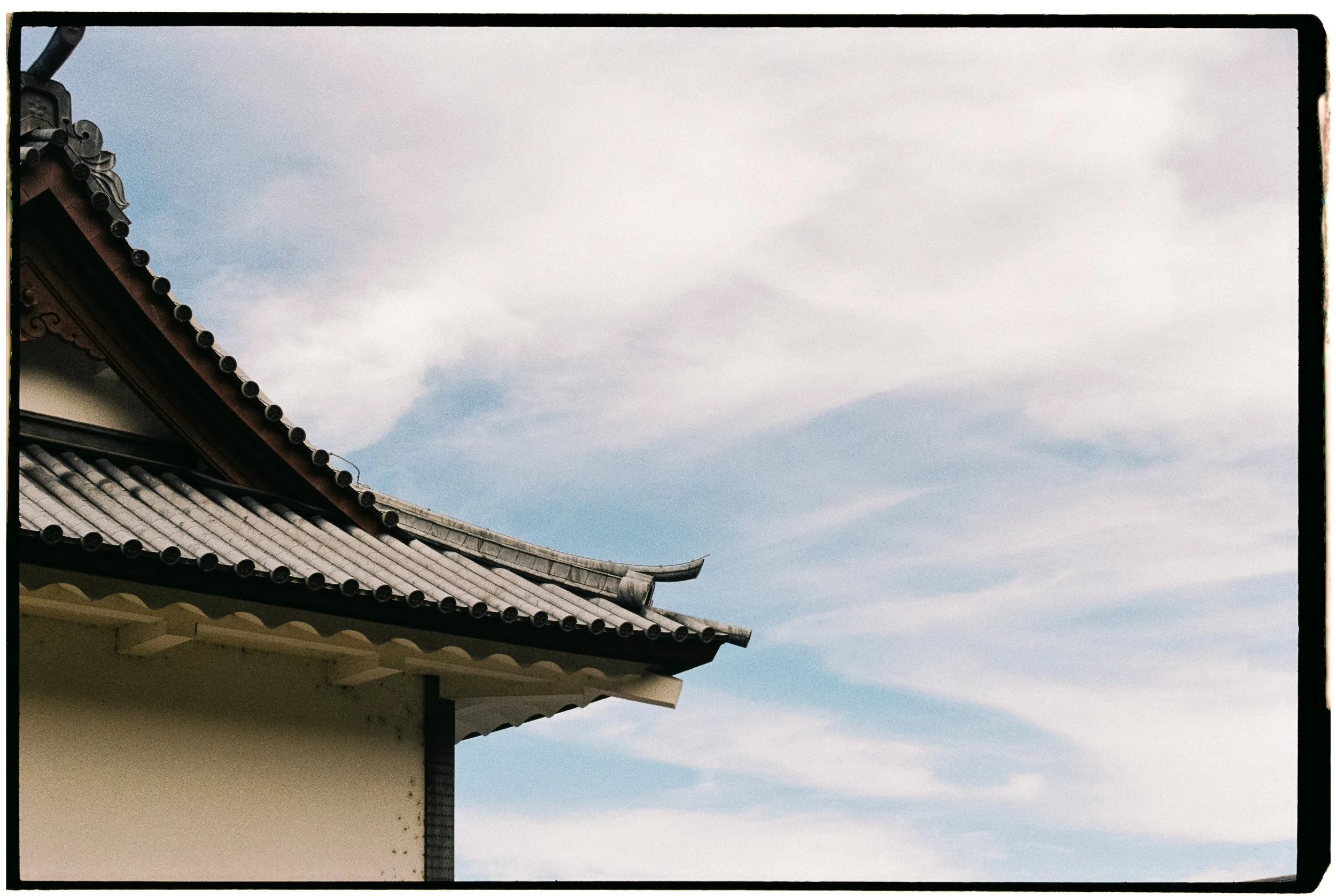 Close-up of traditional Japanese roof with curved tiled eaves against cloudy sky.