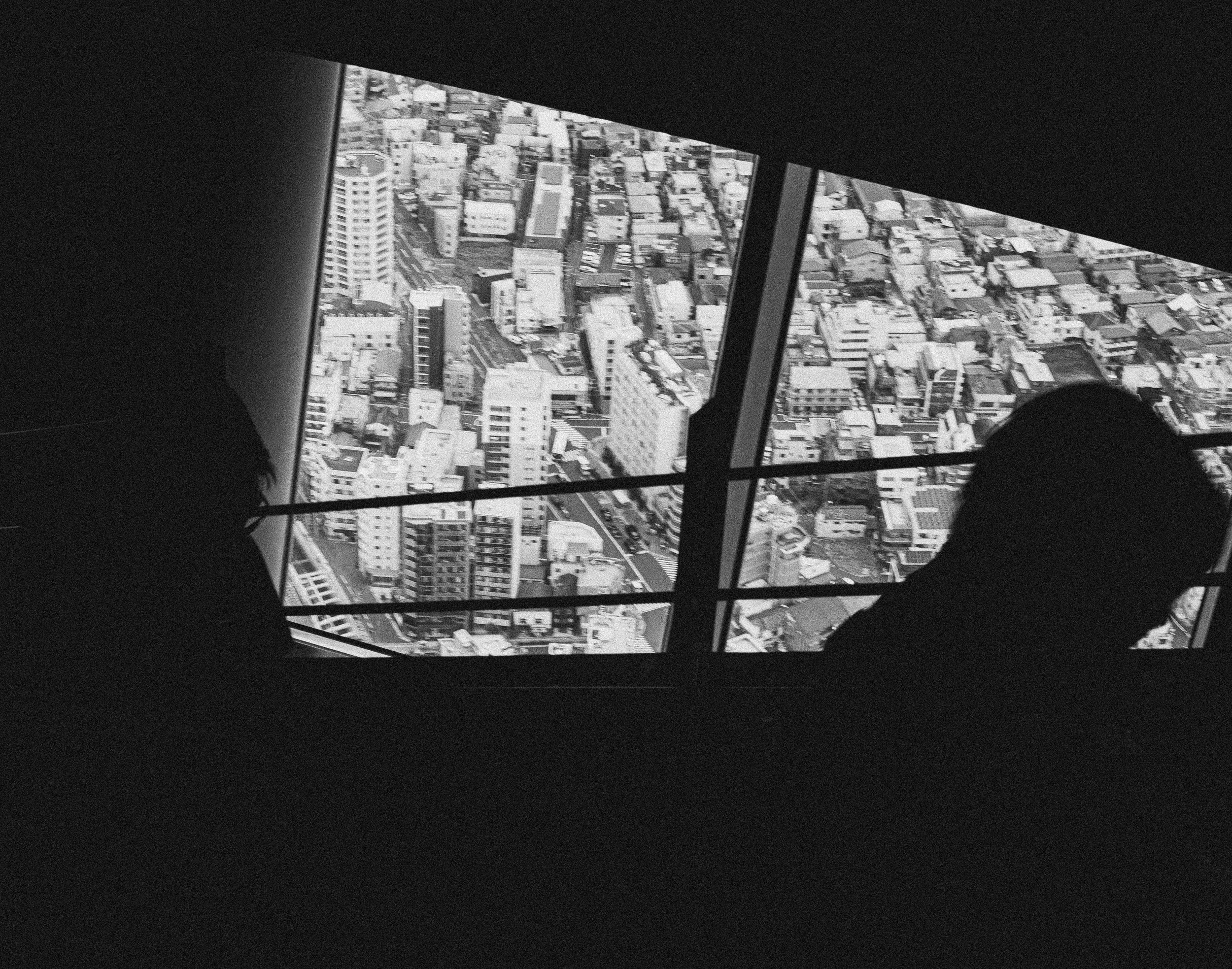 Silhouettes of two people in front of a large window overlooking a cityscape with tall buildings and streets.