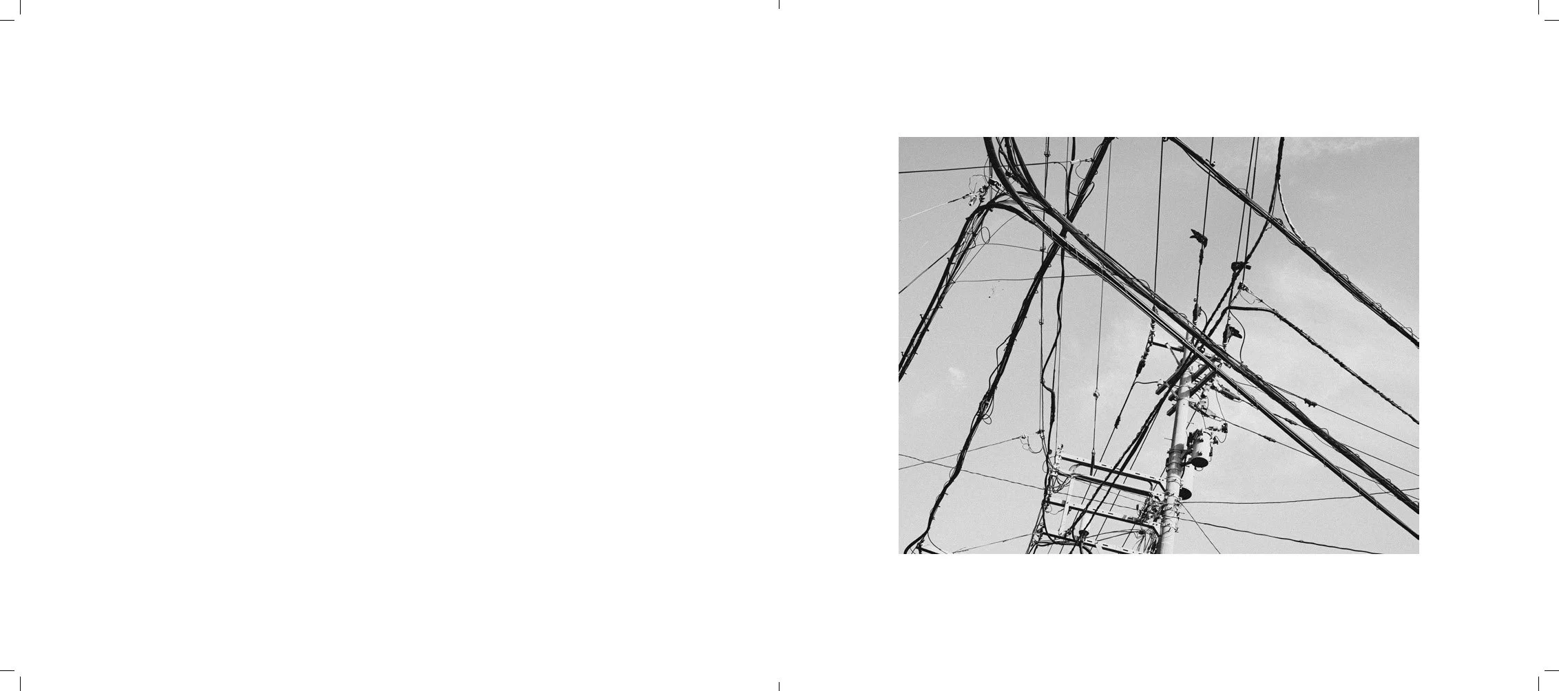 Black and white photo of multiple electrical power lines and utility poles against a cloudy sky.