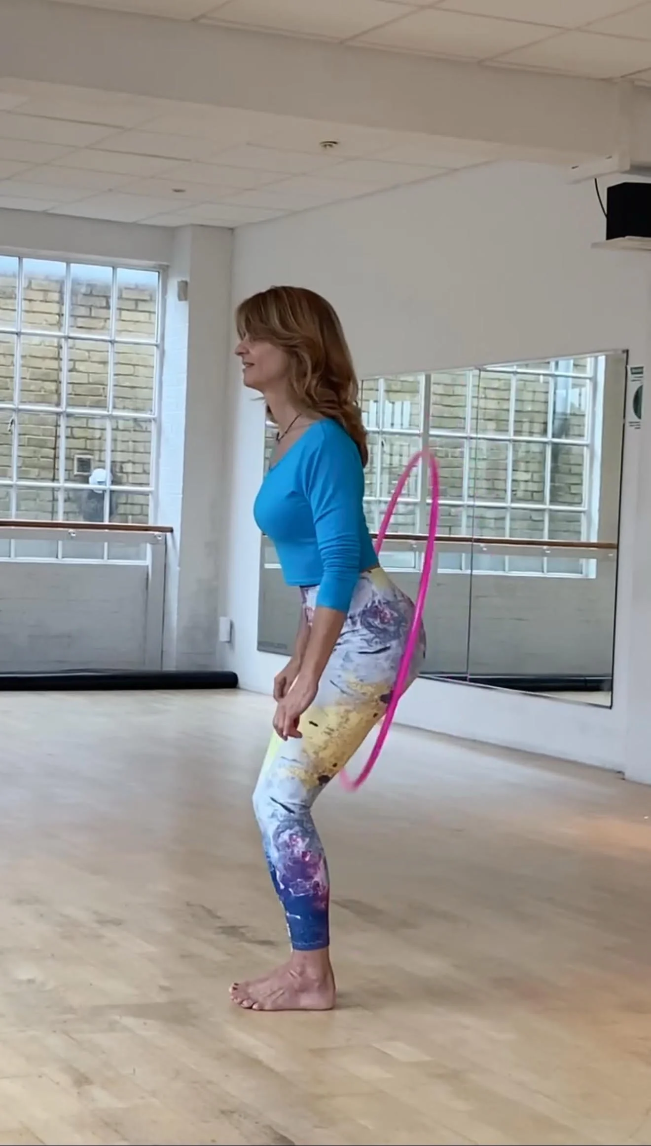 Andrea HulamyHoop winning a Guiness world record in a studio go booty hopping, with a pink hula hoop around her waist, wearing Art Flow Whirleytimes leggings and a blue top.