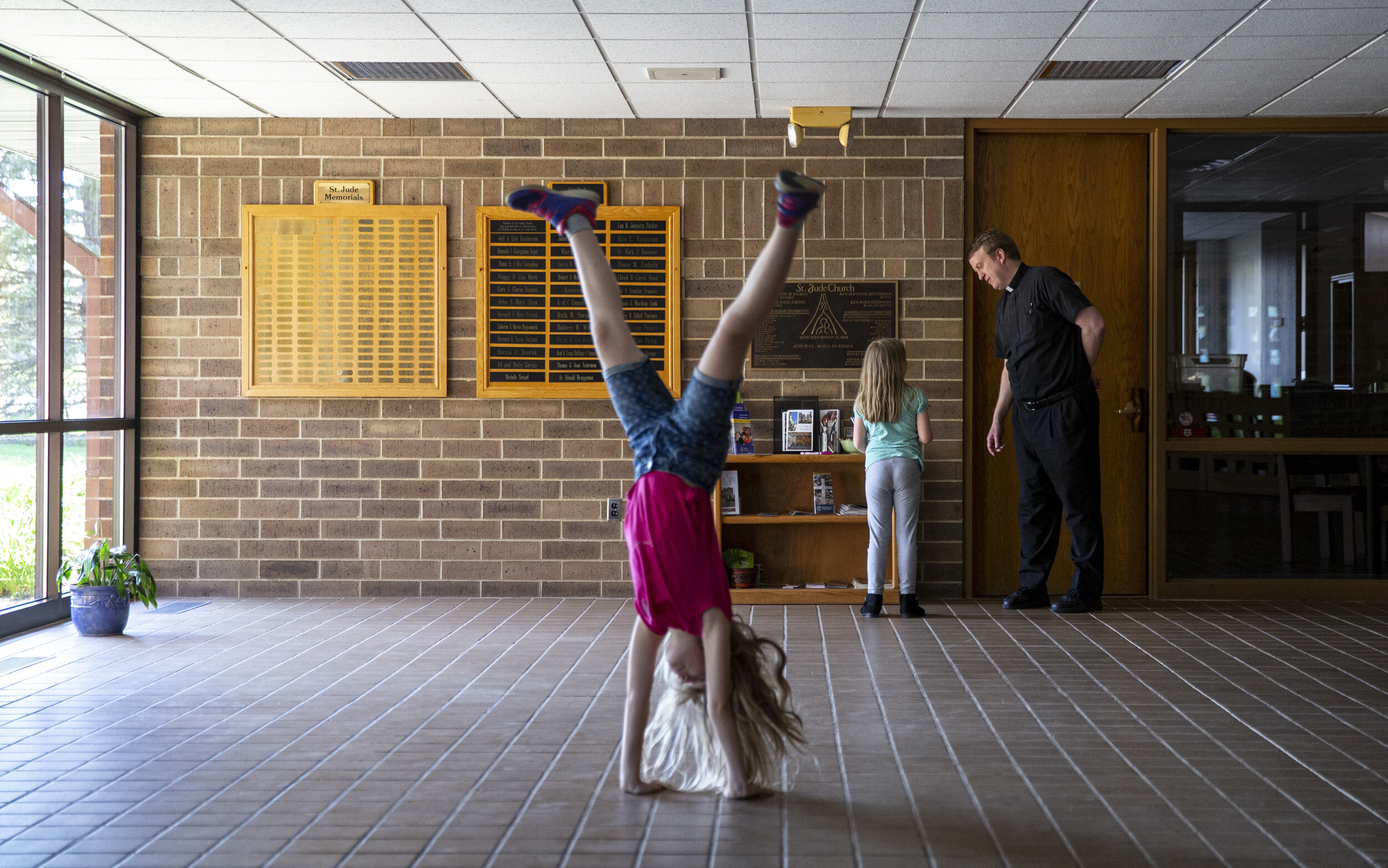  Rev. Mark Murphy talks with Eva Hutchins, 7, as her older sister, Lizzie, 10, does a cartwheel in the lobby at St. Jude’s Catholic Church in Cedar Rapids on Tuesday. The Hutchins’ five daughters had been homeschooling and had not left the house much