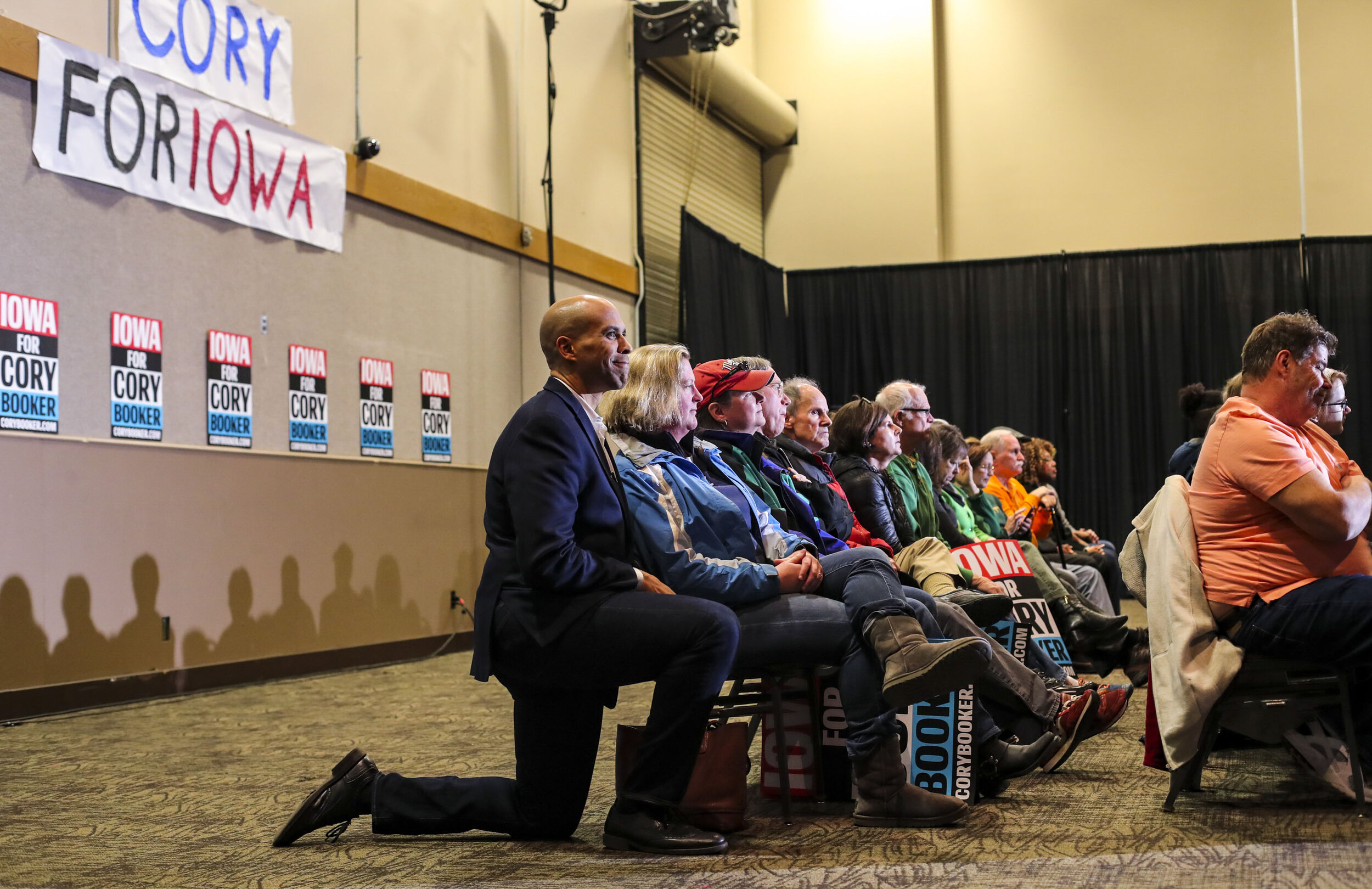  Sen. Cory Booker kneels alongside an attendee sitting in the back row just before he's introduced during a campaign event at the RiverCenter in Davenport, Iowa, Sunday.  