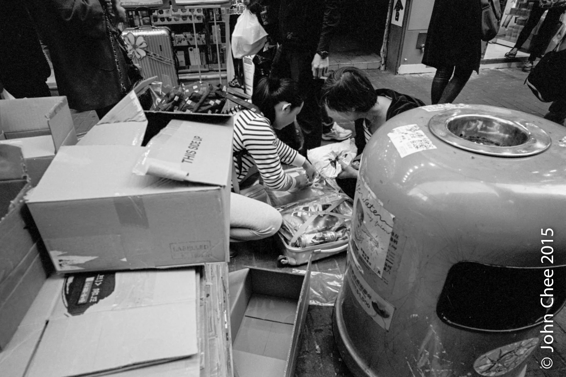Smugglers from China stuffing their suitcases with baby formula, hair shampoo, etc. in the middle of a sidewalk. These items from Hong Kong are popular in China as fake goods available in Chinese stores become health hazards to the general public. (Mong Kok, Hong Kong)
