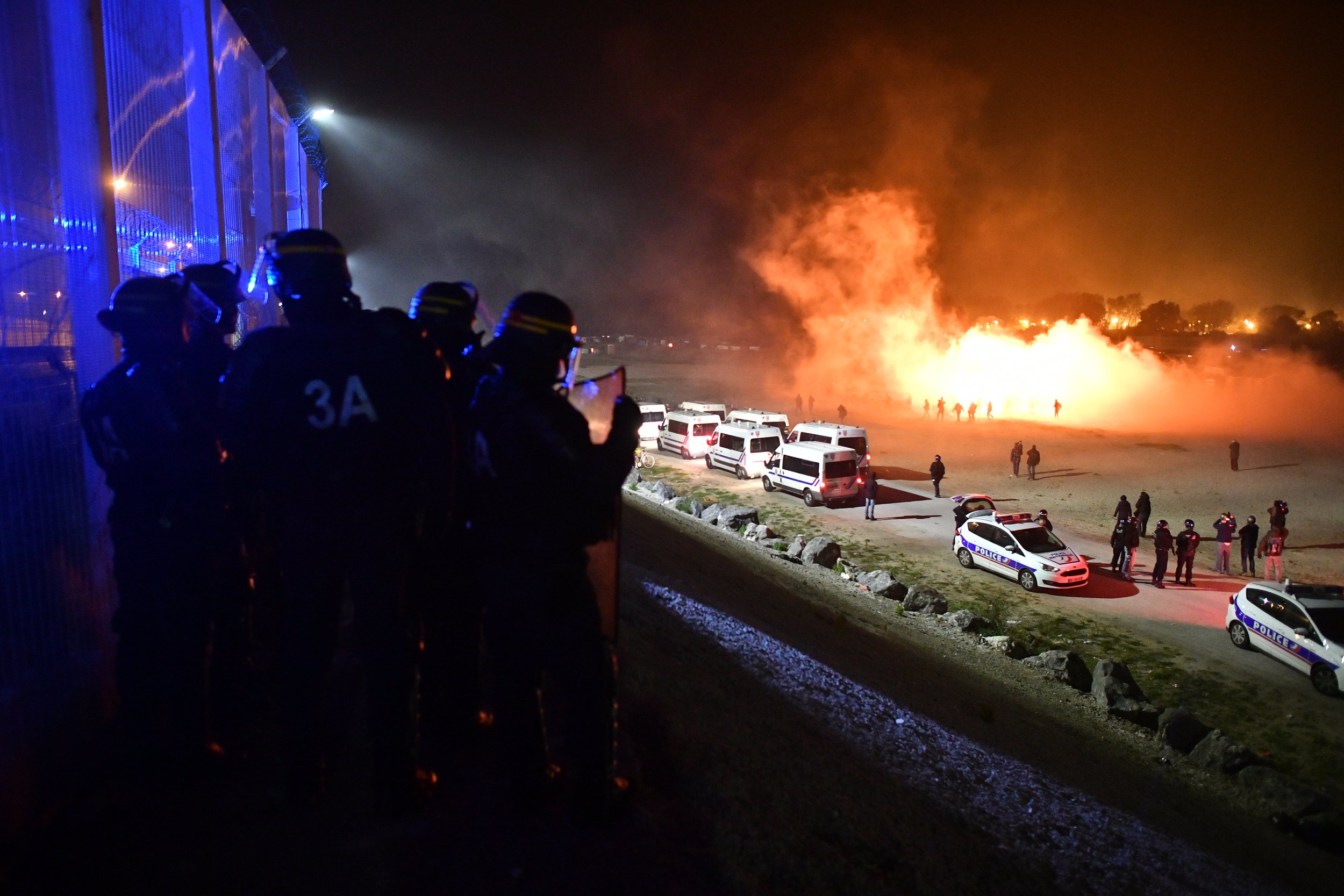 Police watch over the Jungle camp as it burns, the night before eviction.