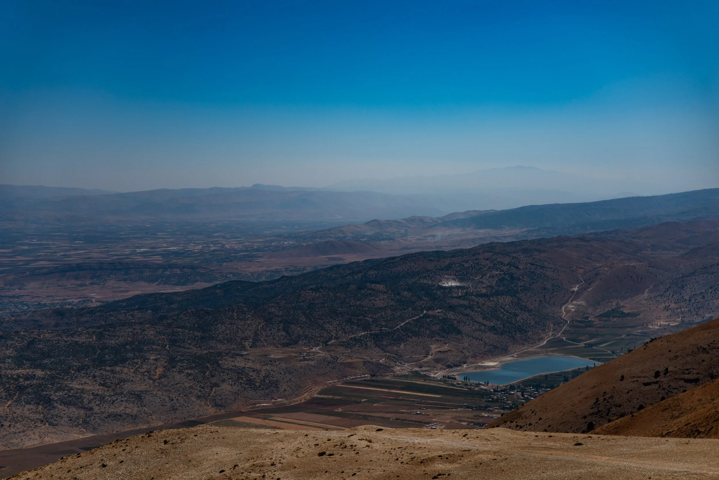 The Beqaa Valley of Lebanon as viewed from a ridge below Qurnat as Sawdā, the highest peak in Lebanon and the Levant. The fertile valley, once known as the bread basket of the Roman empire, is flanked by the Lebanon and Anti-Lebanon Mountains. The g