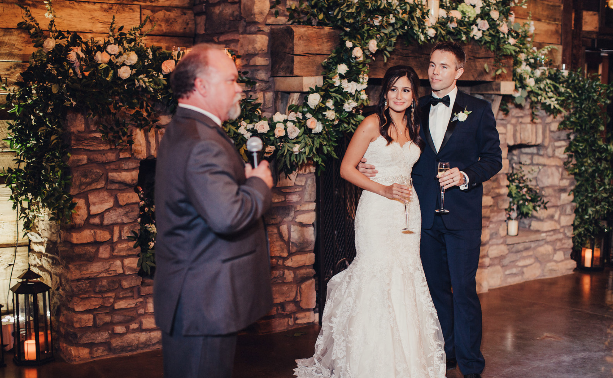 Guest giving a toast in front of the fireplace adorned with a floral and greenery garland by maxit Flower Design in Houston, TX.