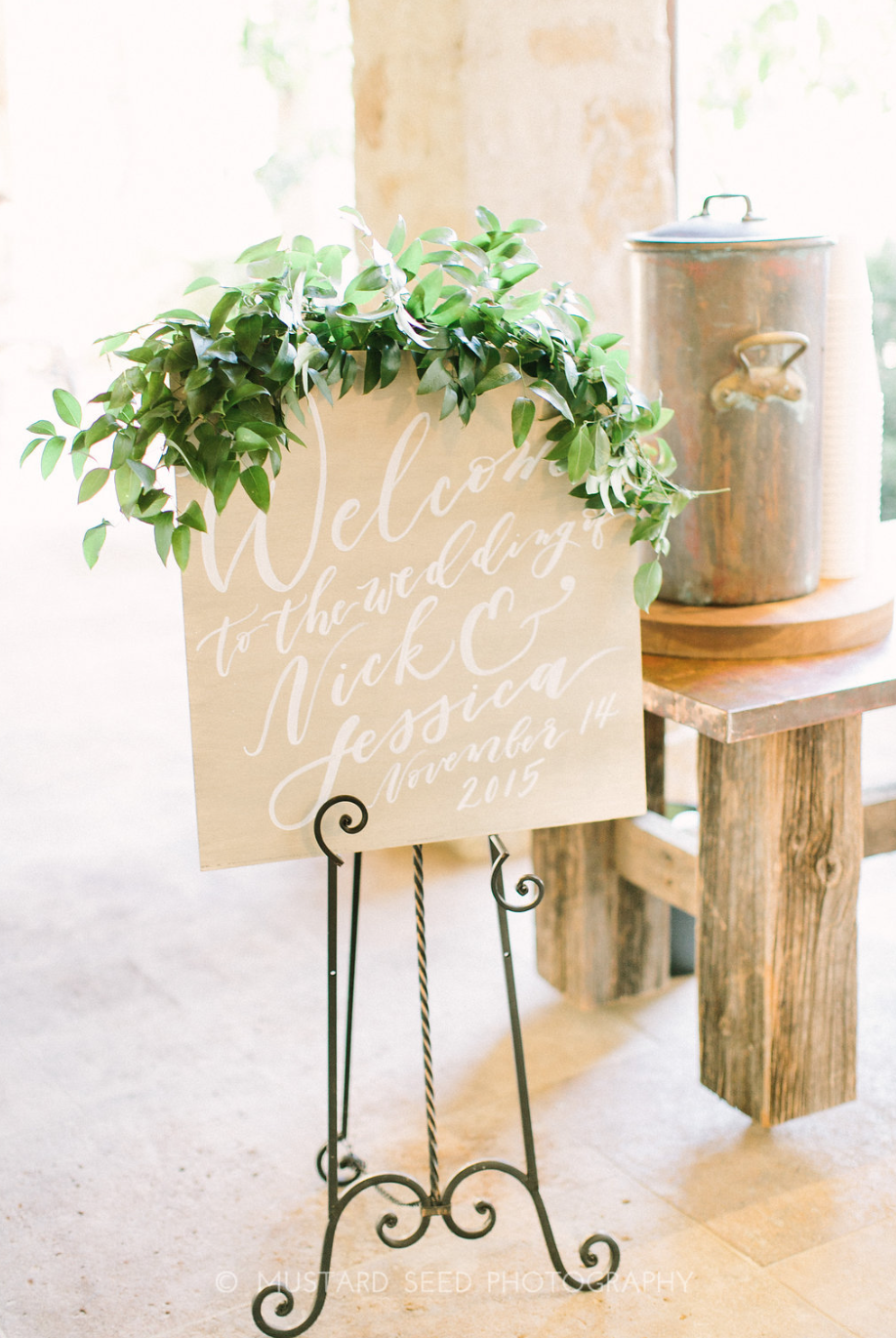 Calligraphy welcome sign draped with greenery by Maxit Flower Design in Houston, TX.