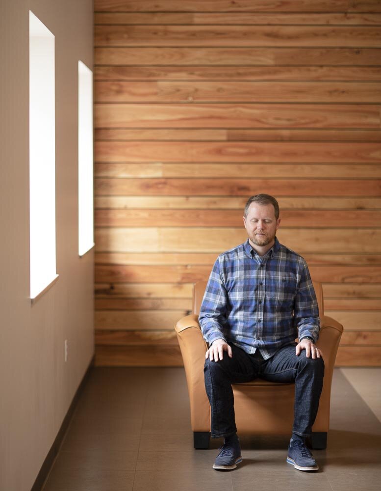 Mediation coach Chad McGehee meditates in quiet room next to two windows.
