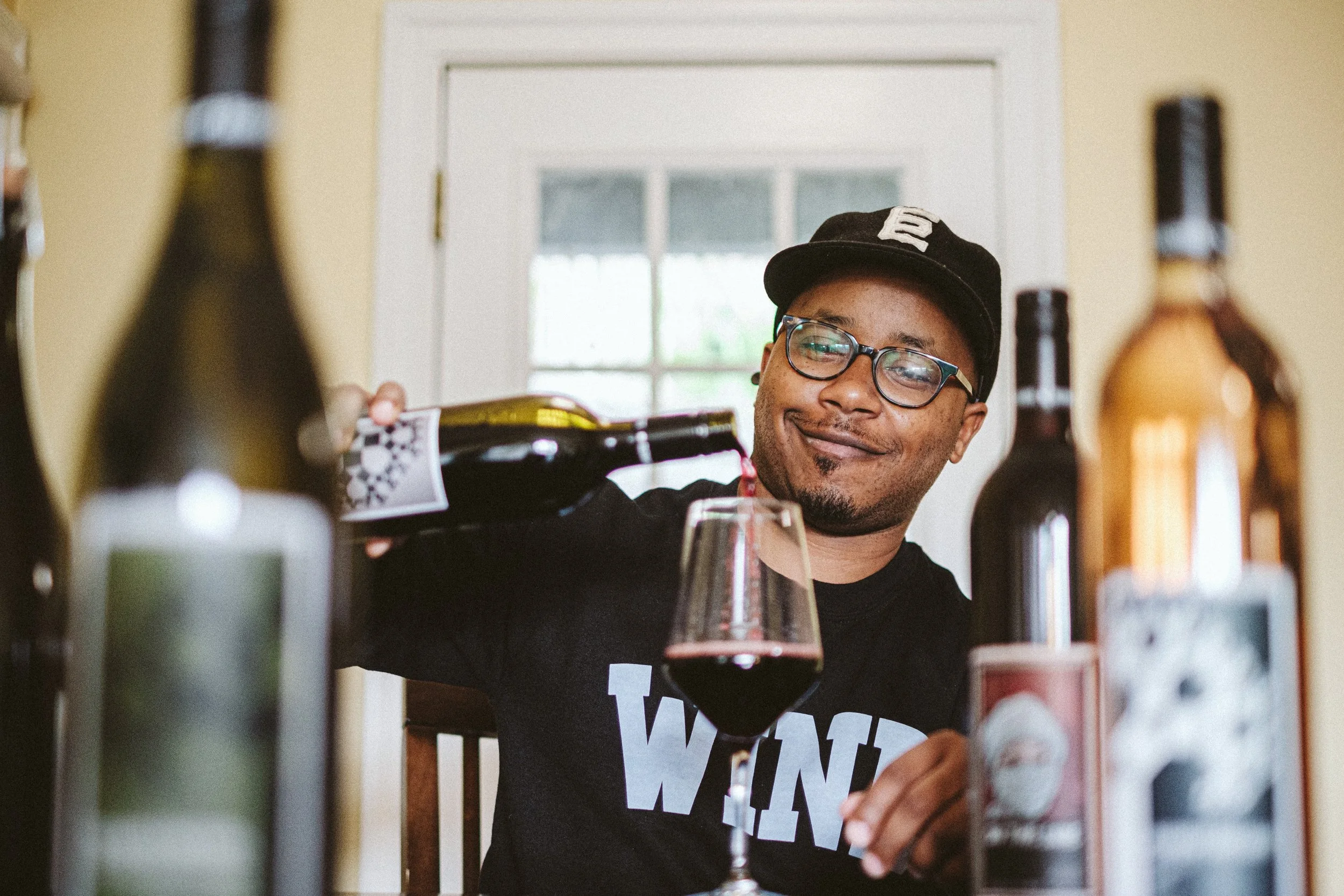 Reggie Leonard smiling through an arrangement of wine bottles and a glass