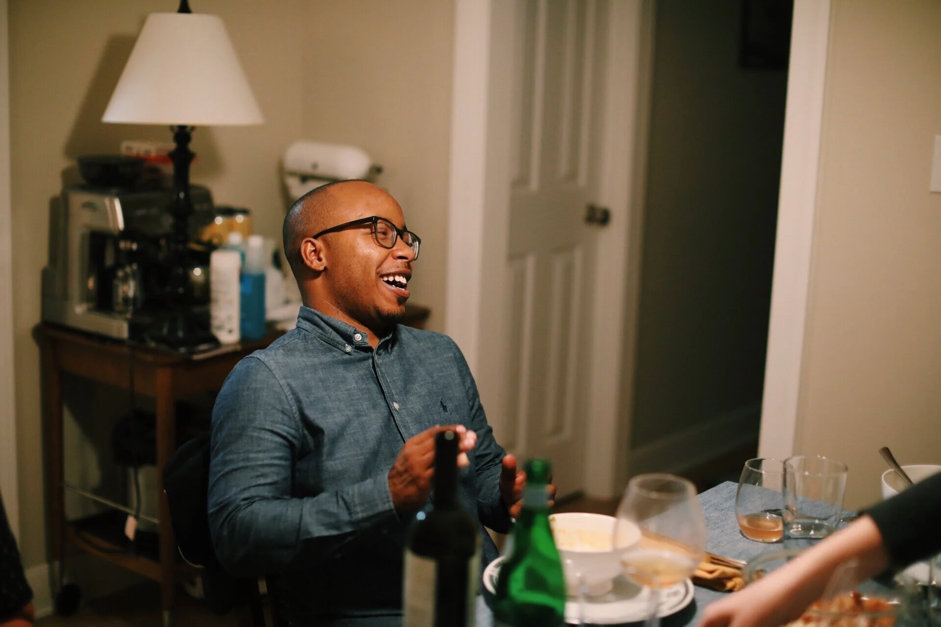 Reggie Leonard laughing at a dinner table, a wine bottle in hand