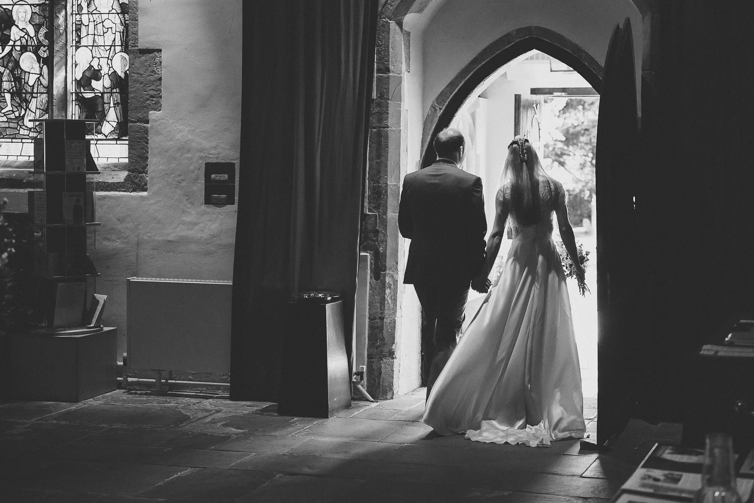 black and white wedding picture of bride and groom leaving old church
