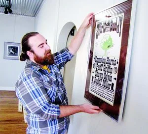   Eliot Reed, owner of Park Place Arts, hangs an exhibition of concert posters, including this Hatch 3-color screen print. Live music comes to the gallery Saturday evening with a free concert by Michael Buratto and Evan Hock.  