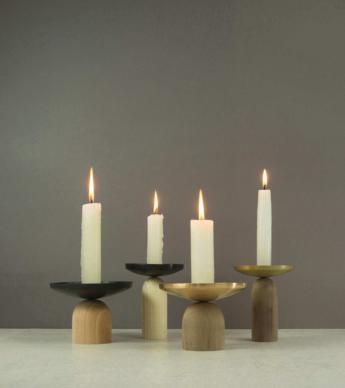 BLUB CANDLE HOLDERS / 2017 BOLIA The concept was to design a set of candle holders that contain the spilling wax and the mess of a candle as it melts away when lit up. The soft and clean curves of solid wood and the metal dish create a very complimenting expression. They have three variations in the wood base and metal top. The wood base comes in walnut, ash and beech, the top dish is in Copper, Brass or Anodized Aluminium. This makes for about 9 combinations. One can hold the wood base to move around without burning the skin with the melting wax. And the tactile feel of the wood is quite pleasant. The base and top are screwed to each other for the ease of cleaning and maintenance. The dish can be cleaned by placing it upside down on a paper in the heated oven. The candle holders have a trick detail at the union of base and top which almost makes it appear as if it’s resting on the tip, almost defying gravity. The screw which joins the metal dish and the wood base has a pin on top; this also helps the candle stand upright. Materials : Walnut / Beech / Ash wood base and the dish are in Copper / Brass / Anodized Aluminium.