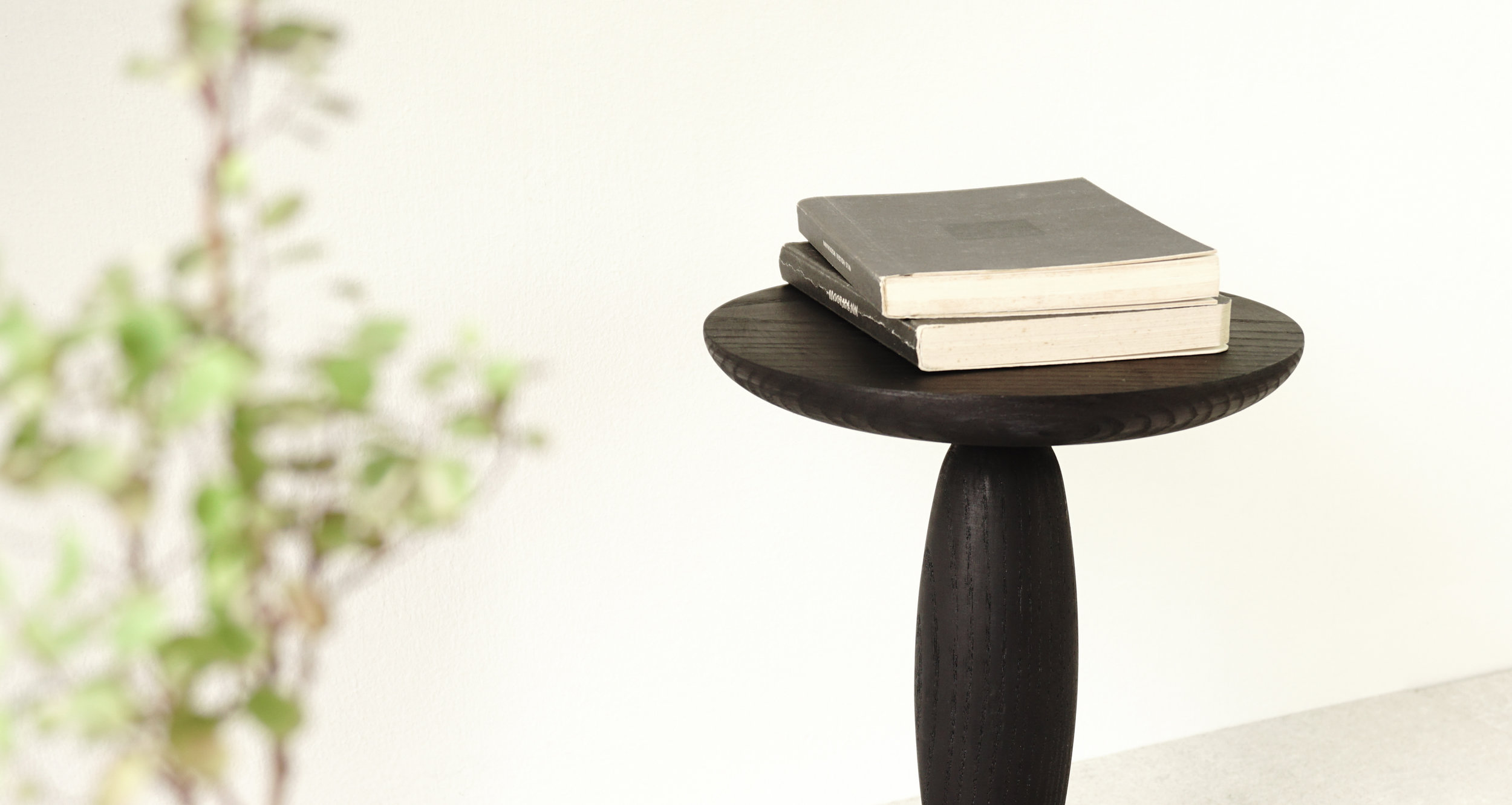 BLAK Side table The black and golden from the visuals of ancient artefacts of Egypt and Persia provoked this series. One of the first in that is 'BLAK Stool'. It is quite 'Primitive' in its expression of form and finish, the way the brilliant golden finish contrasts with the rough texture of black wood, relatively emphasising its texture more. It provokes certain nostalgia of the ancient era. The form and use of gunmetal and Stained ash-wood makes it something which could have been made several centuries ago, if it was done as an essential object with not much decoration, resorting to the available tools of the age and materials. The soft bubble elements in wood are constricted with small metal rings at the junctions, breaking and articulating the shape.