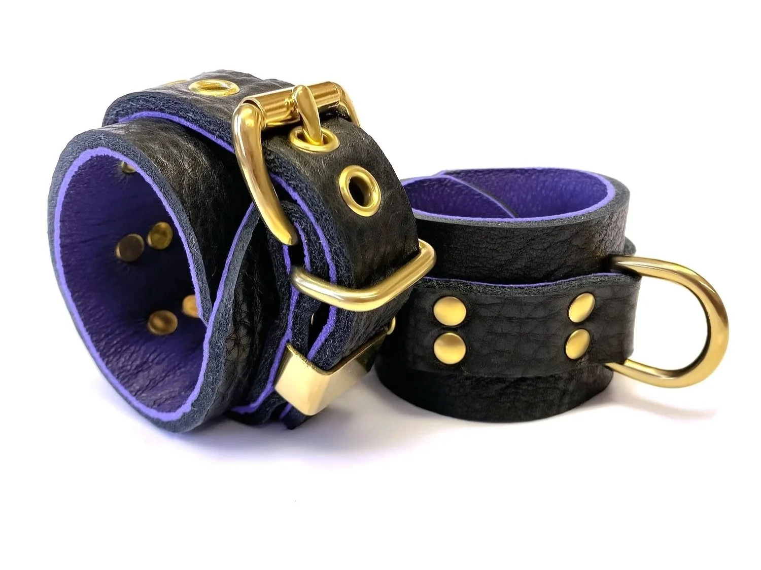 pair of soft black restraints lined in purple leather with brass fittings