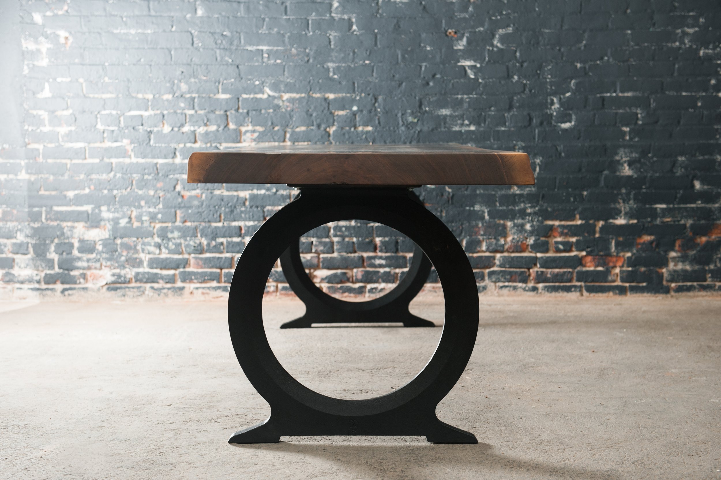 A modern wooden and metal table placed on a concrete floor against a dark brick wall.