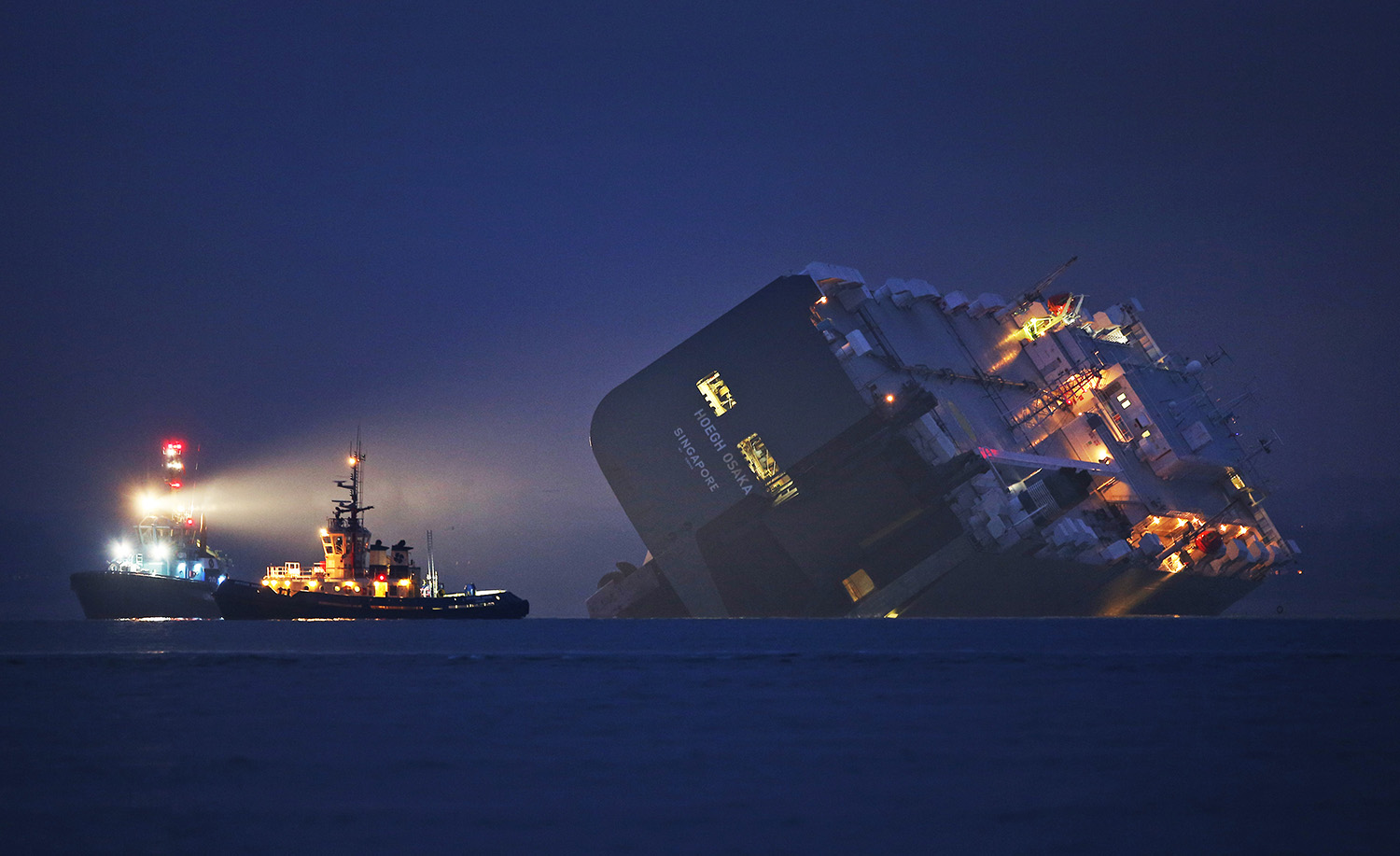 A salvage tug lights the hull of the stricken Hoegh Osaka cargo ship after it ran aground on a sand bank in the Solent, England. January 4, 2015.