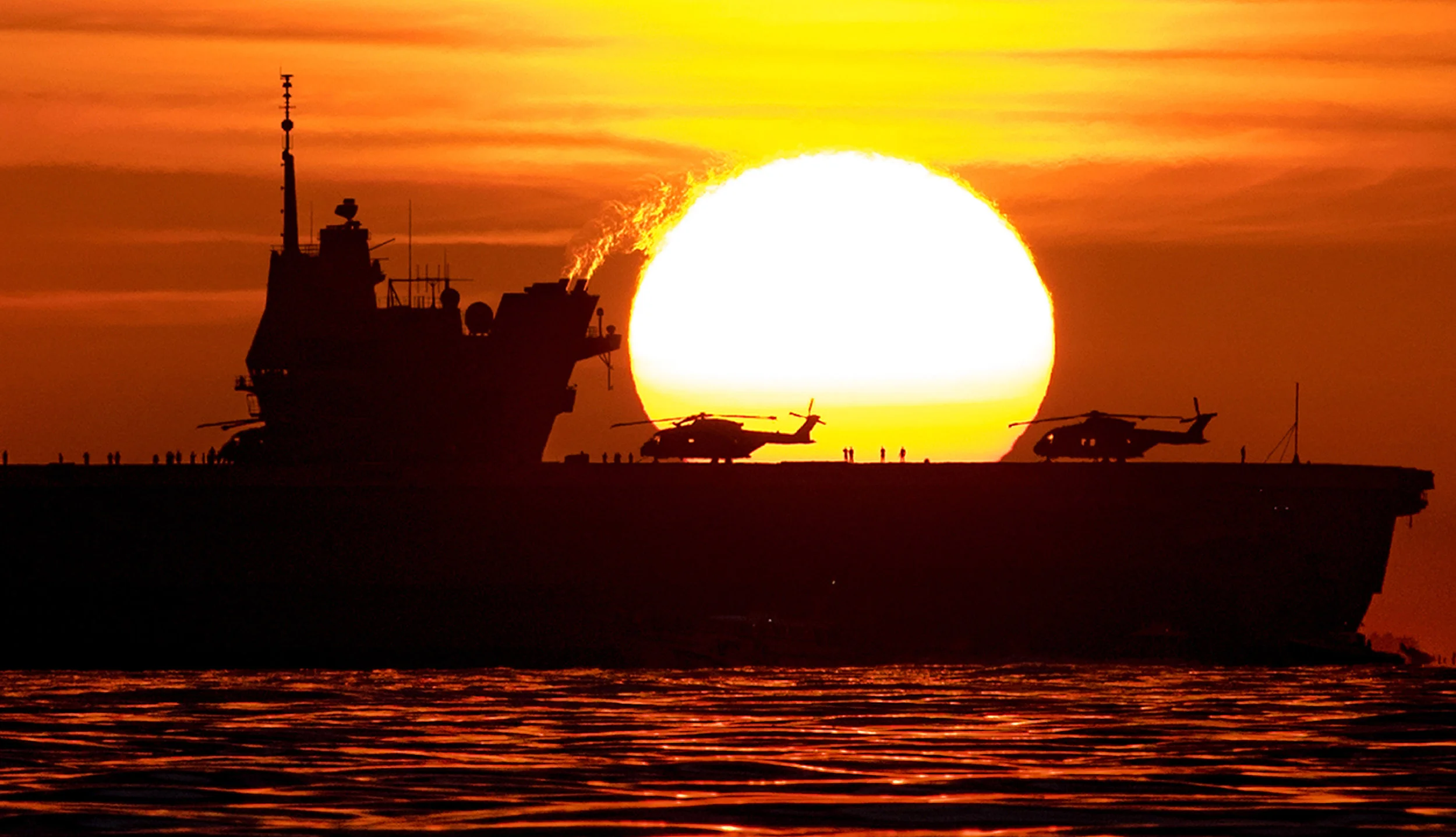 The sun rises behind the Royal Navy's new aircraft carrier HMS Queen Elizabeth as she nears her home port of Portsmouth for the first time. August 16, 2017. Portsmouth.