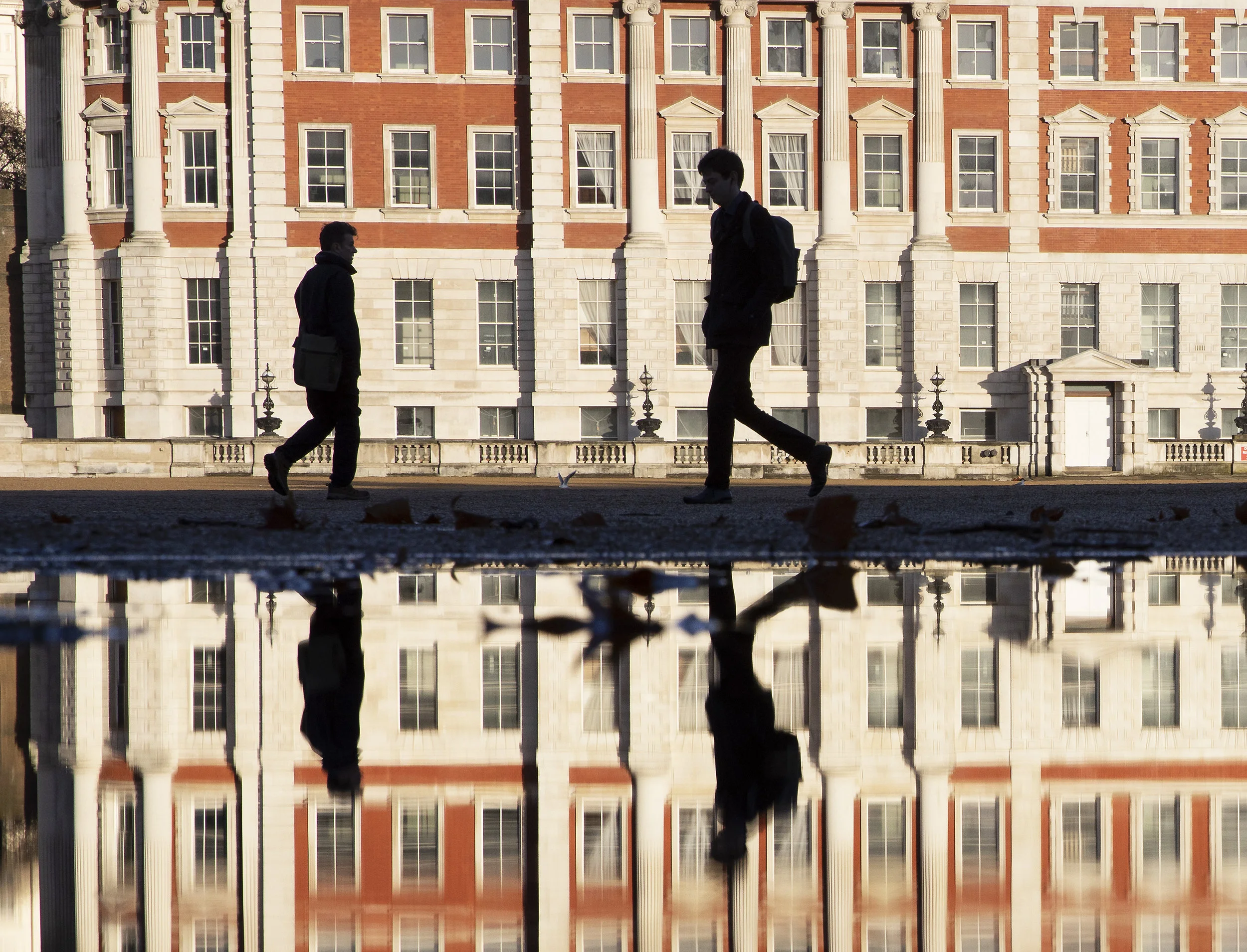 People making their way to work across Horse Guards Parade are reflected in a puddle and silhouetted against a sunlit Admiralty building in London. December 17, 2018.