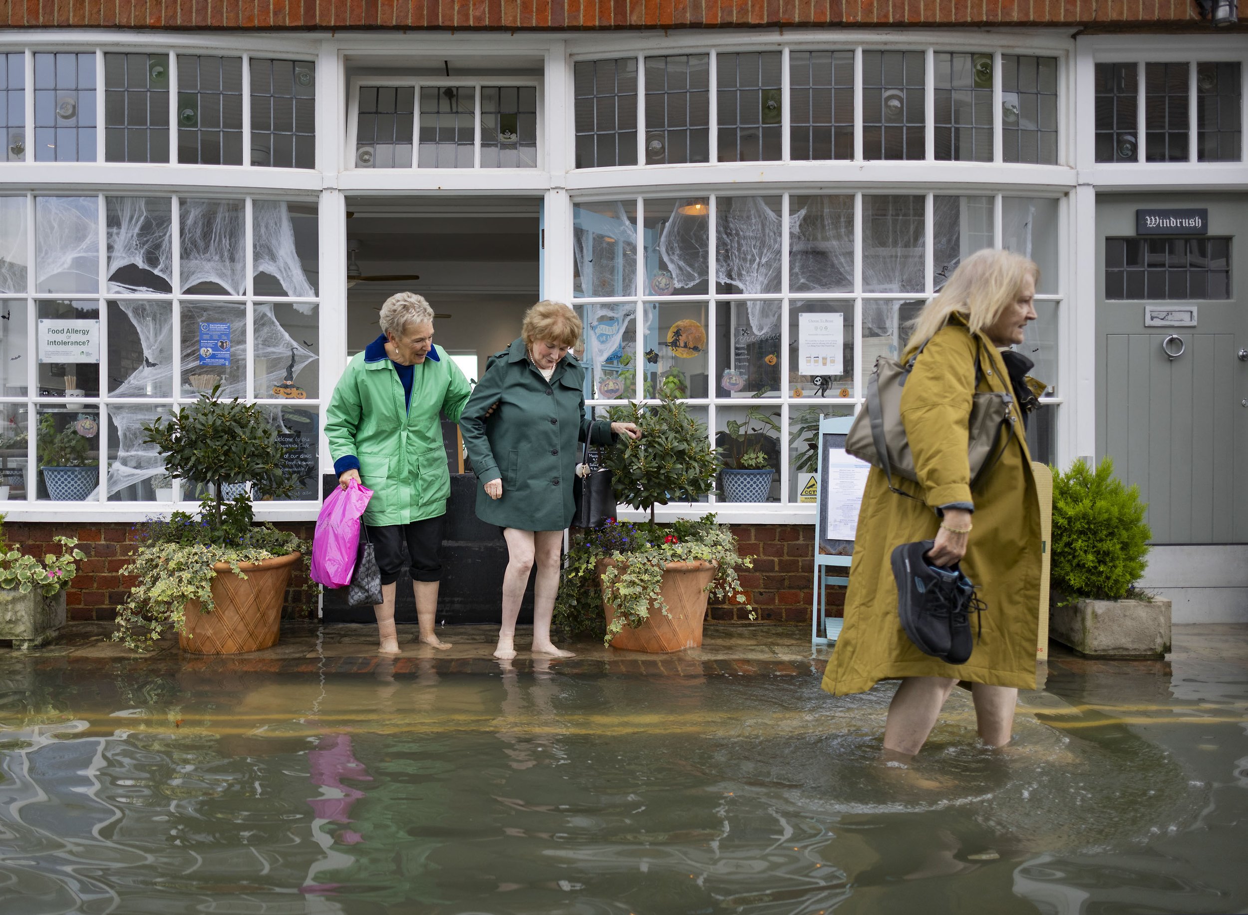 People leaving Shoreside Cafe wade through high-tide floodwater at Bosham in West Sussex on October 30, 2023.