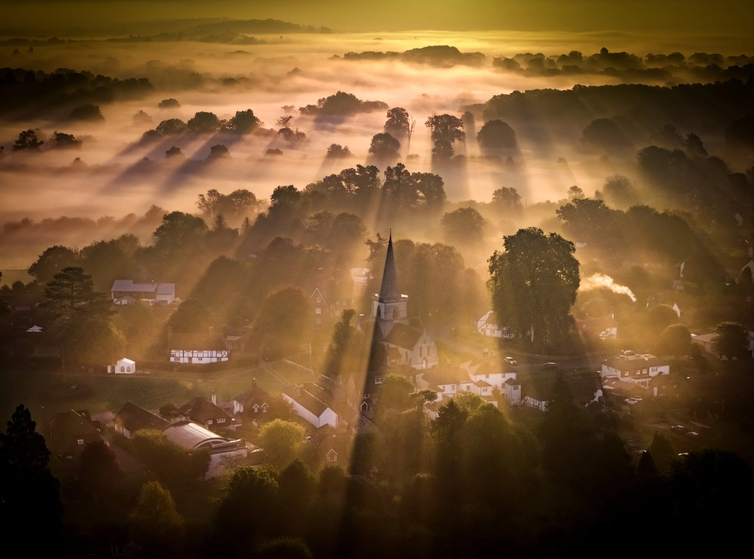 Rays of the misty sunrise swathe Christ Church in the village of Brockham in Surrey on September 29, 2025.