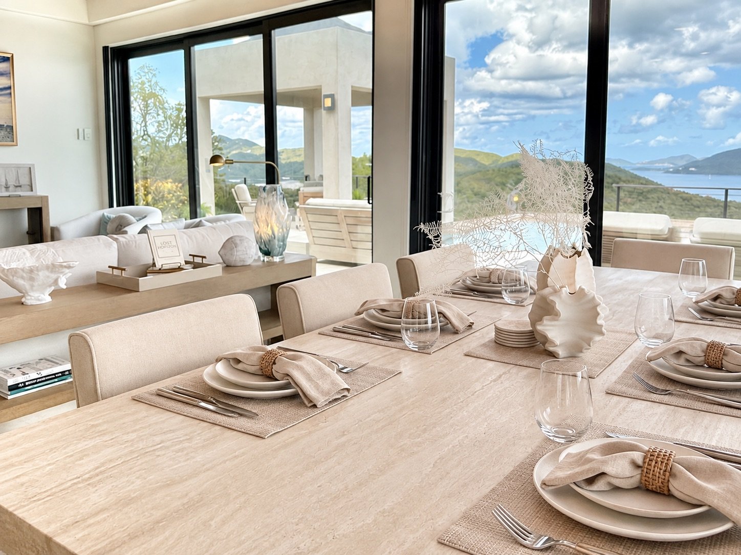 A fully staged dining table with layered neutral place settings and a St. John view