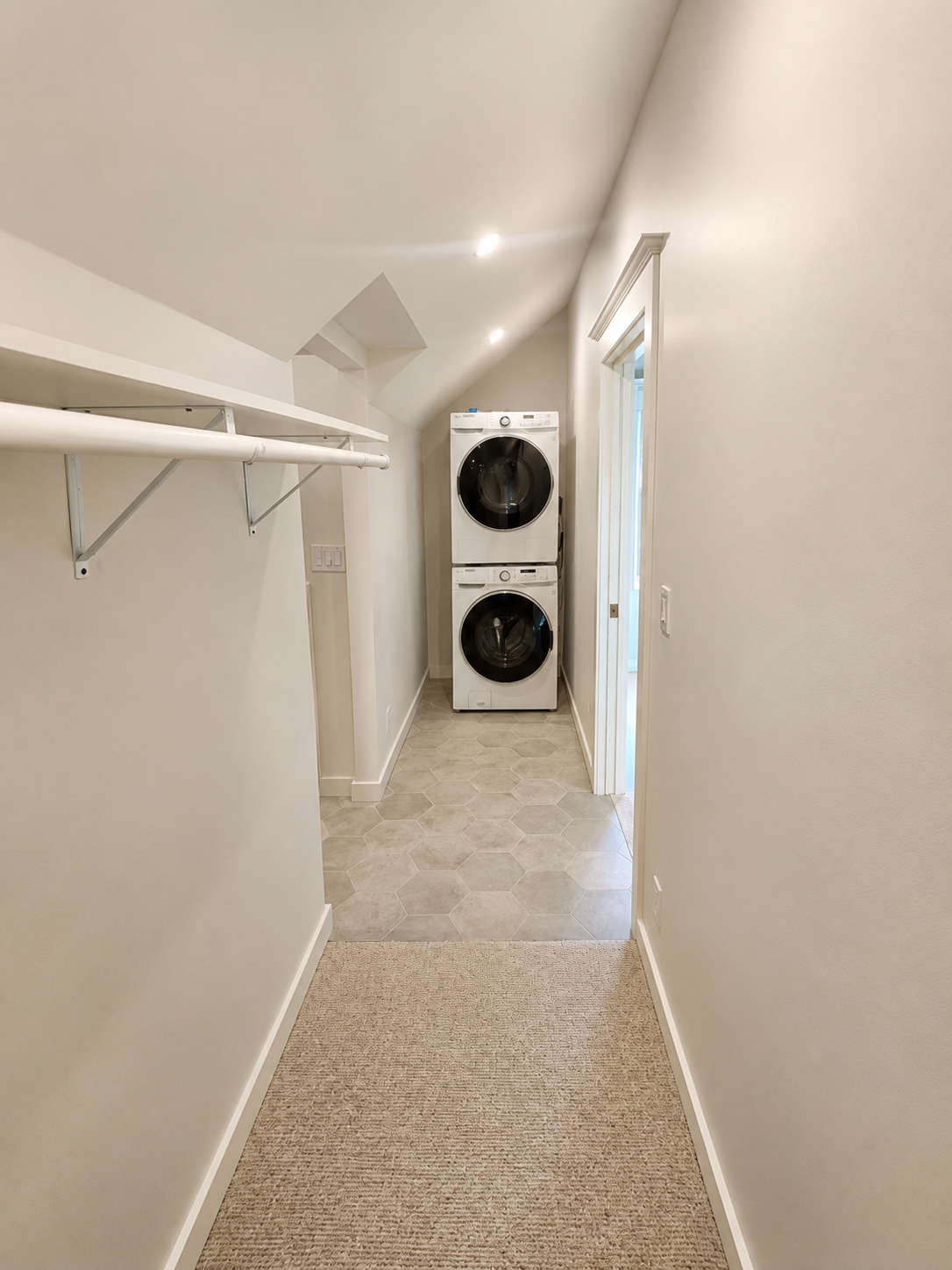 Newly framed laundry room with stacked washer and dryer, tile flooring, and built-in storage as part of a primary suite renovation.
