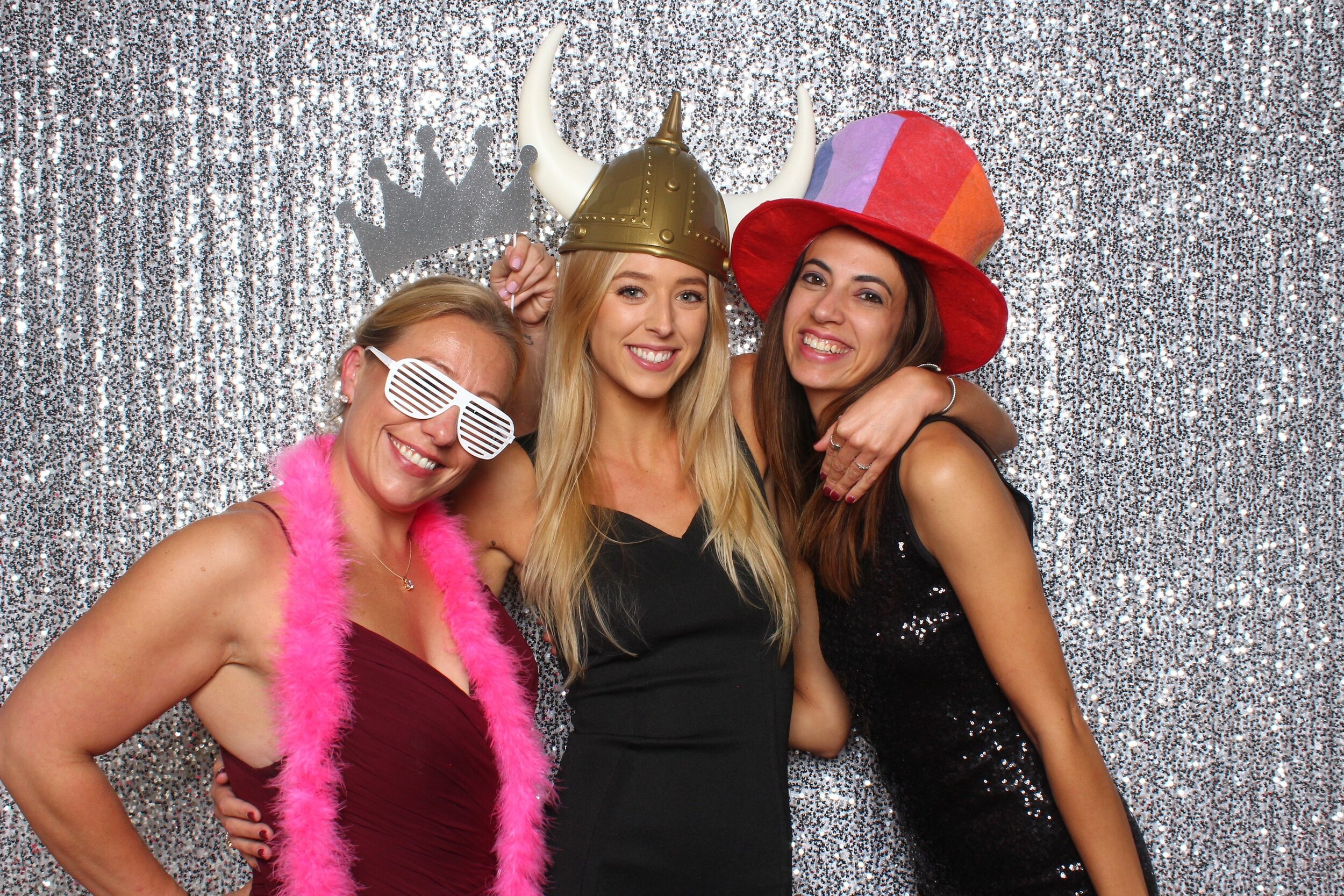  Three women in formal attire and silly props posing for a photo booth picture. 