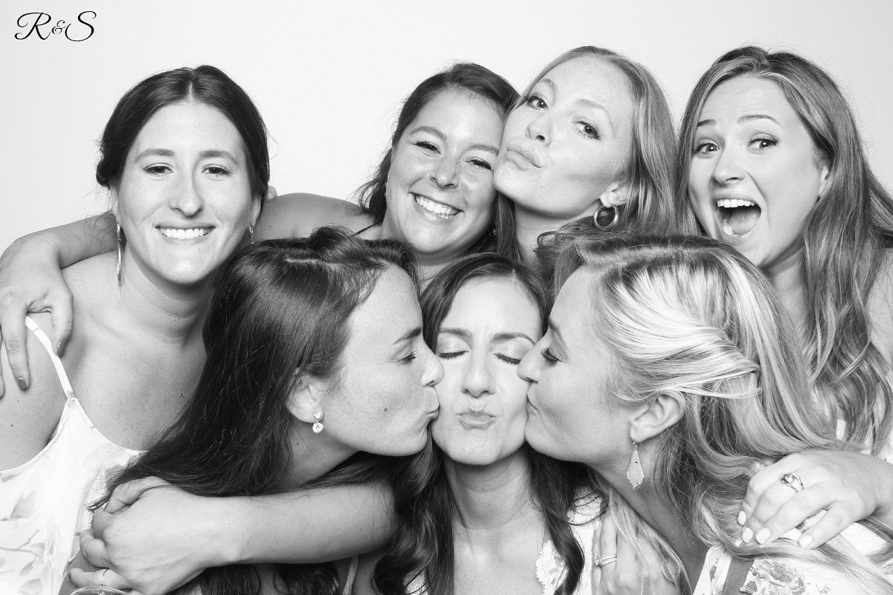  A bridal party bunched together in a photo booth with their arms around each other’s shoulders. 