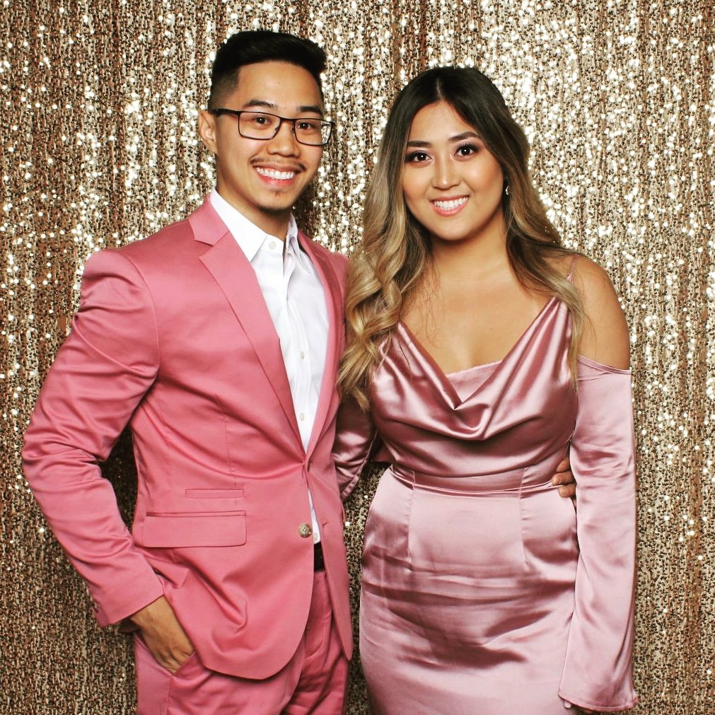  A man and woman in pink formal attire posing in front of a sparkled backdrop. 
