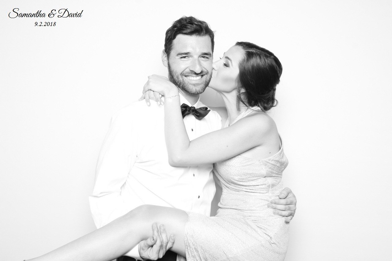  A man holding a woman kissing him on the cheek in a photo booth. 