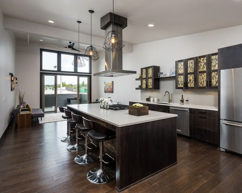 Open kitchen with a dark island, bar stools and cage pendants, tall windows beyond