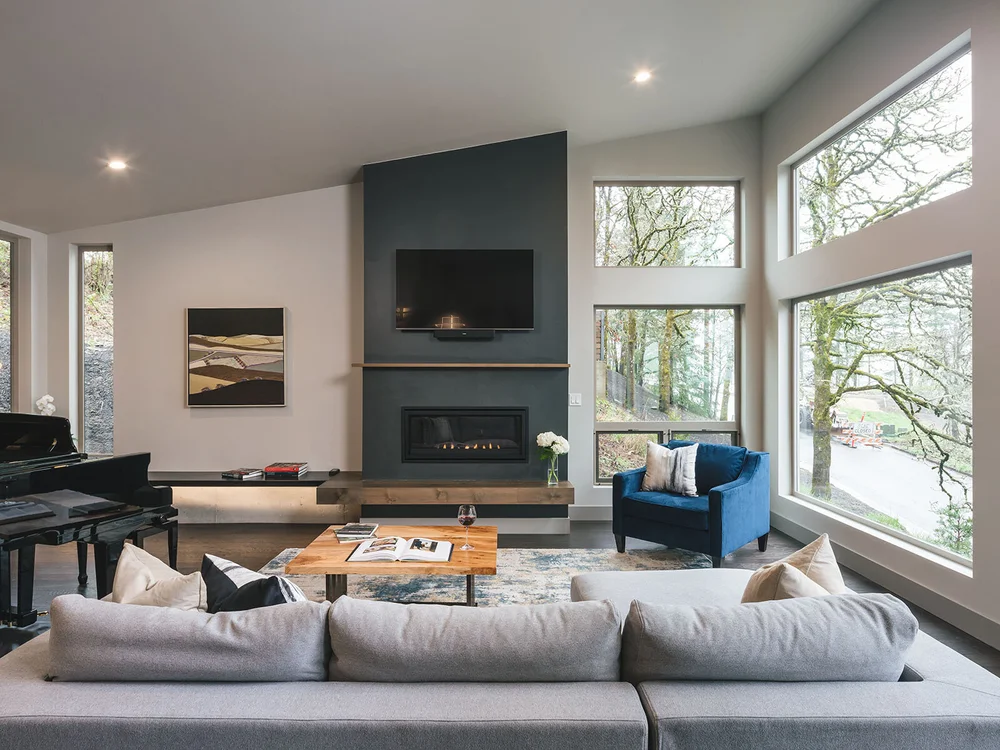 Living room with a dark fireplace wall and tall windows onto oak trees