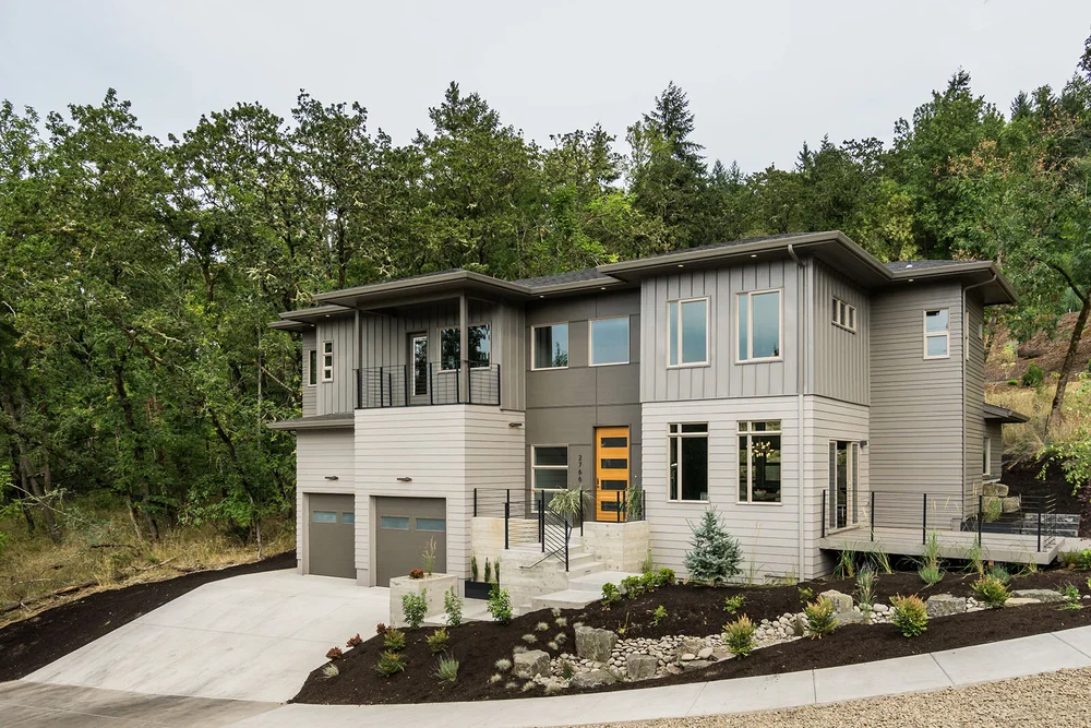 Two-storey contemporary home with mixed siding set against a wooded hill