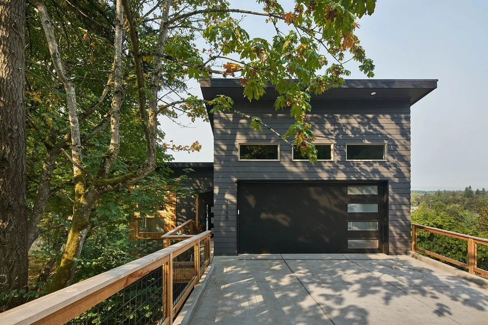 Dark modern house seen from a deck among oak trees