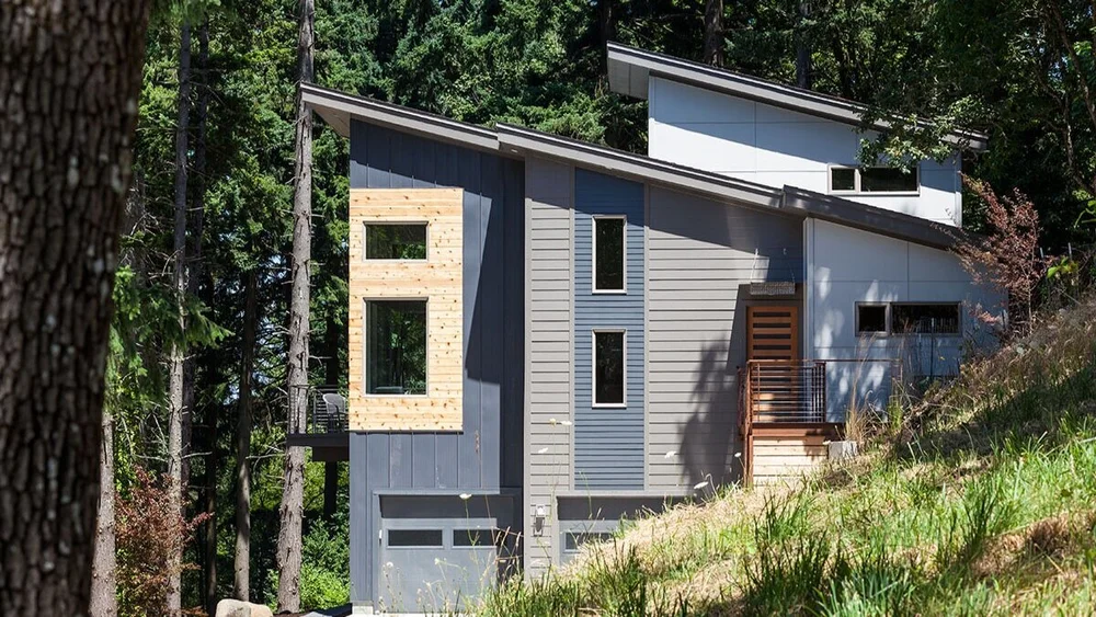 Modern hillside house with dark siding and a tall window bay