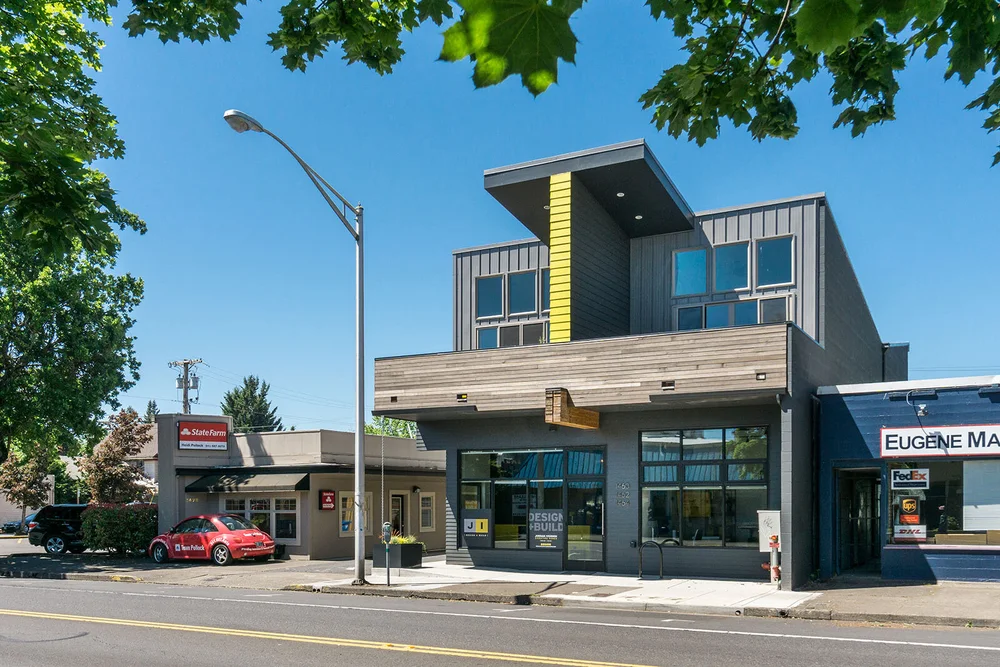Street view of a modern mixed-use building with a yellow accent panel