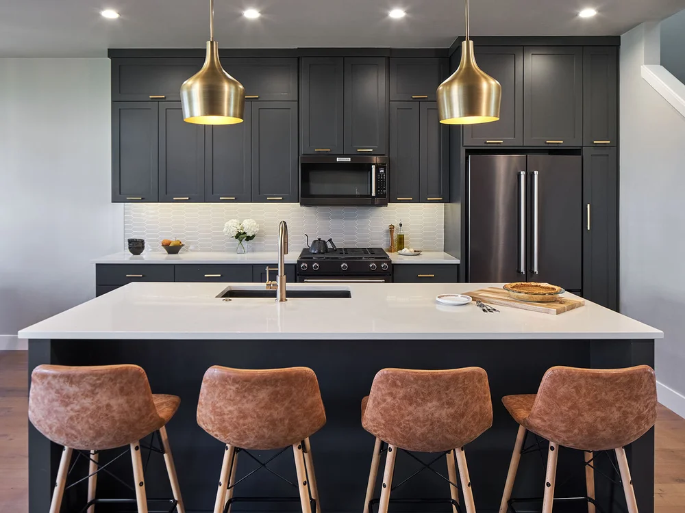 Kitchen with dark cabinets, brass pendants and leather counter stools