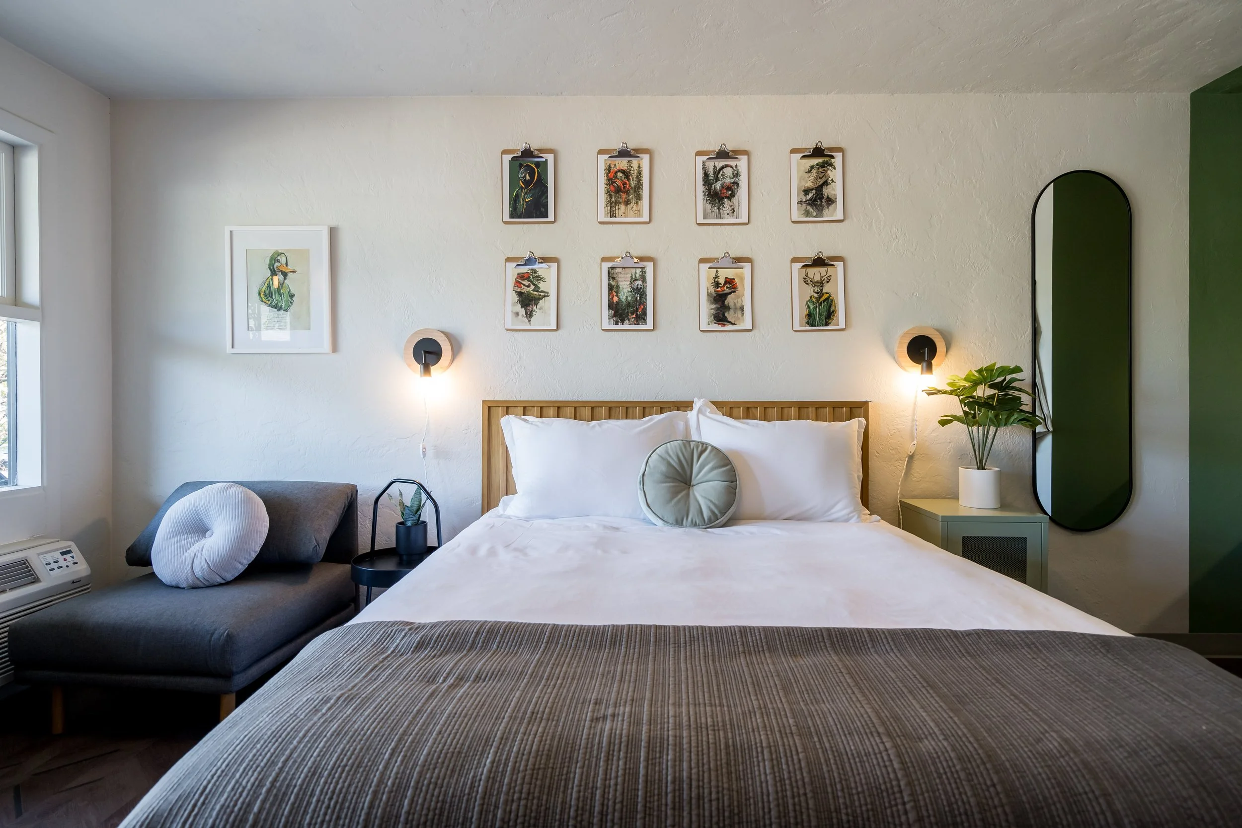 Boutique guest room with a green accent wall, framed artwork, and layered bedding