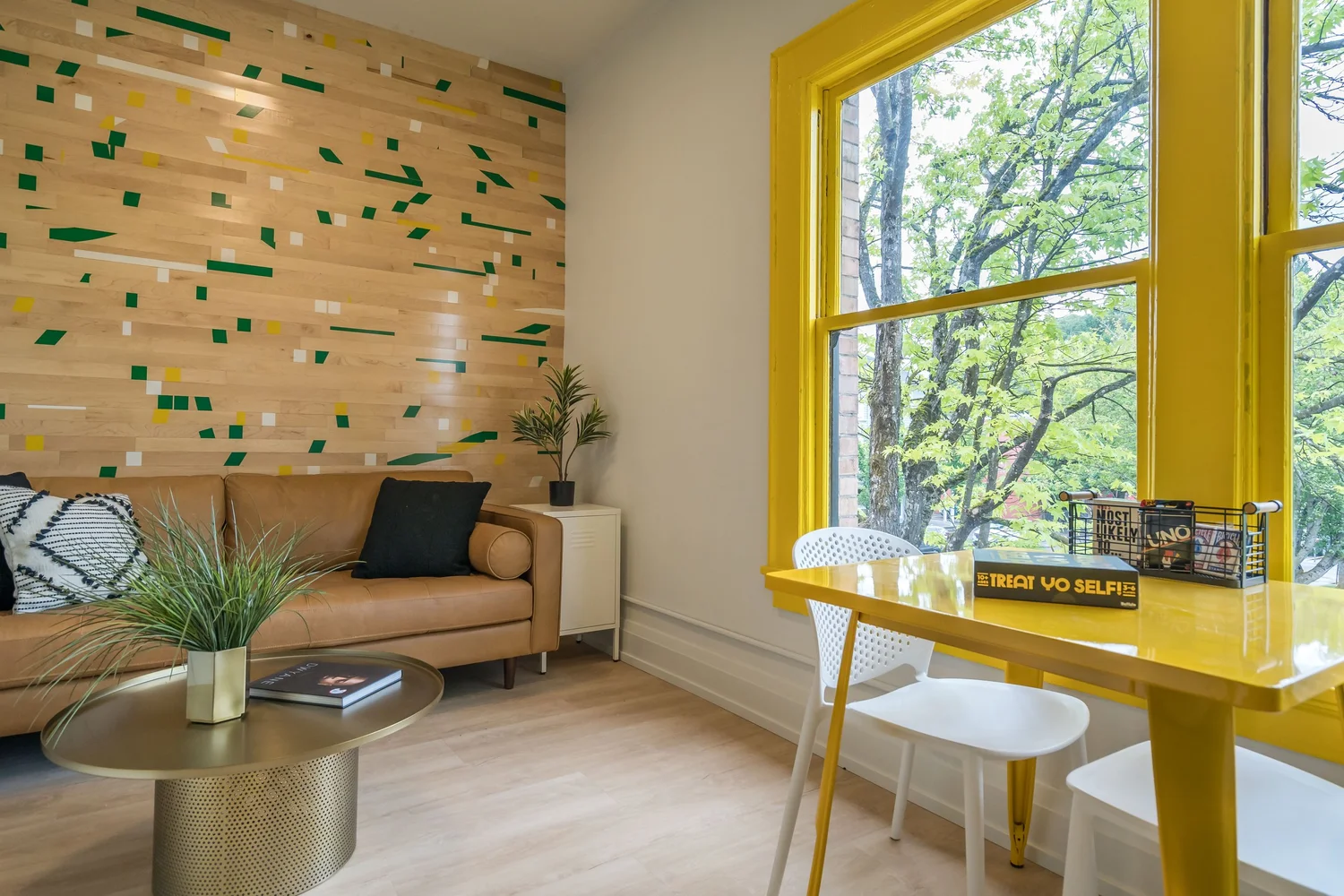 Sitting room with a bright yellow window frame and desk, and a wood slat wall with green inlays