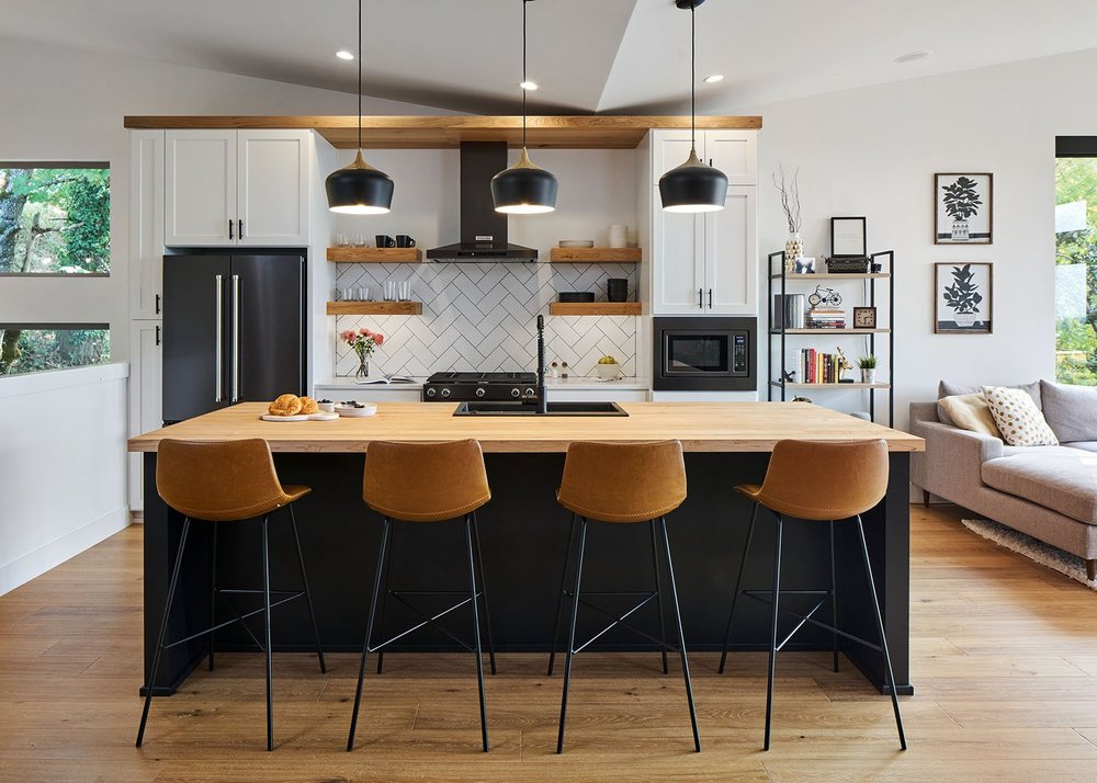 Kitchen with a black island, butcher-block top, cognac leather stools and three black pendants